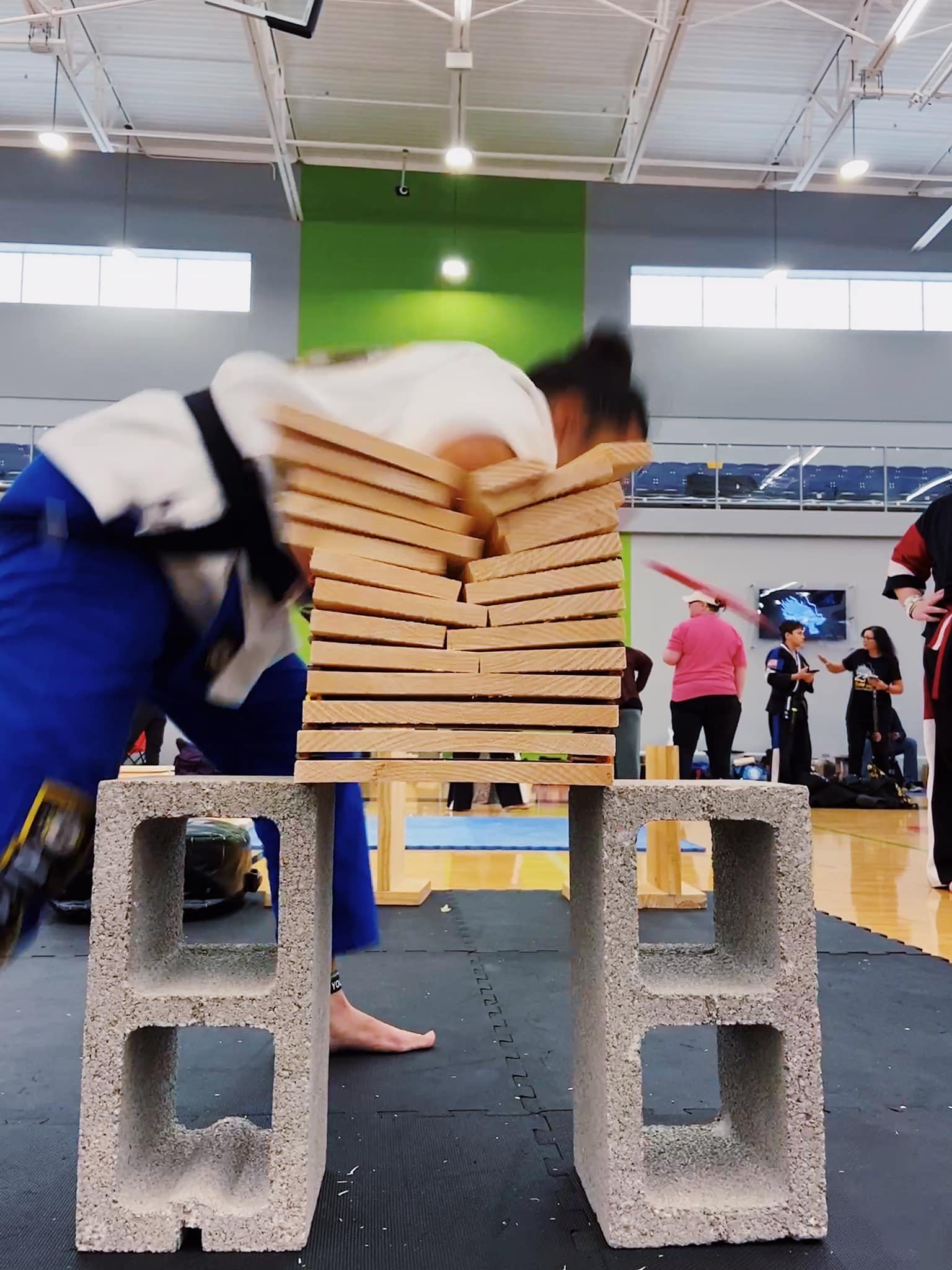 Person breaking wooden boards in a martial arts demonstration indoors, using their head to strike the boards supported by concrete blocks.
