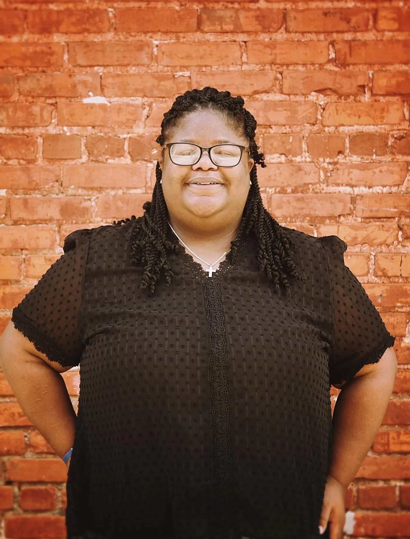 Person wearing black blouse standing against a brick wall.