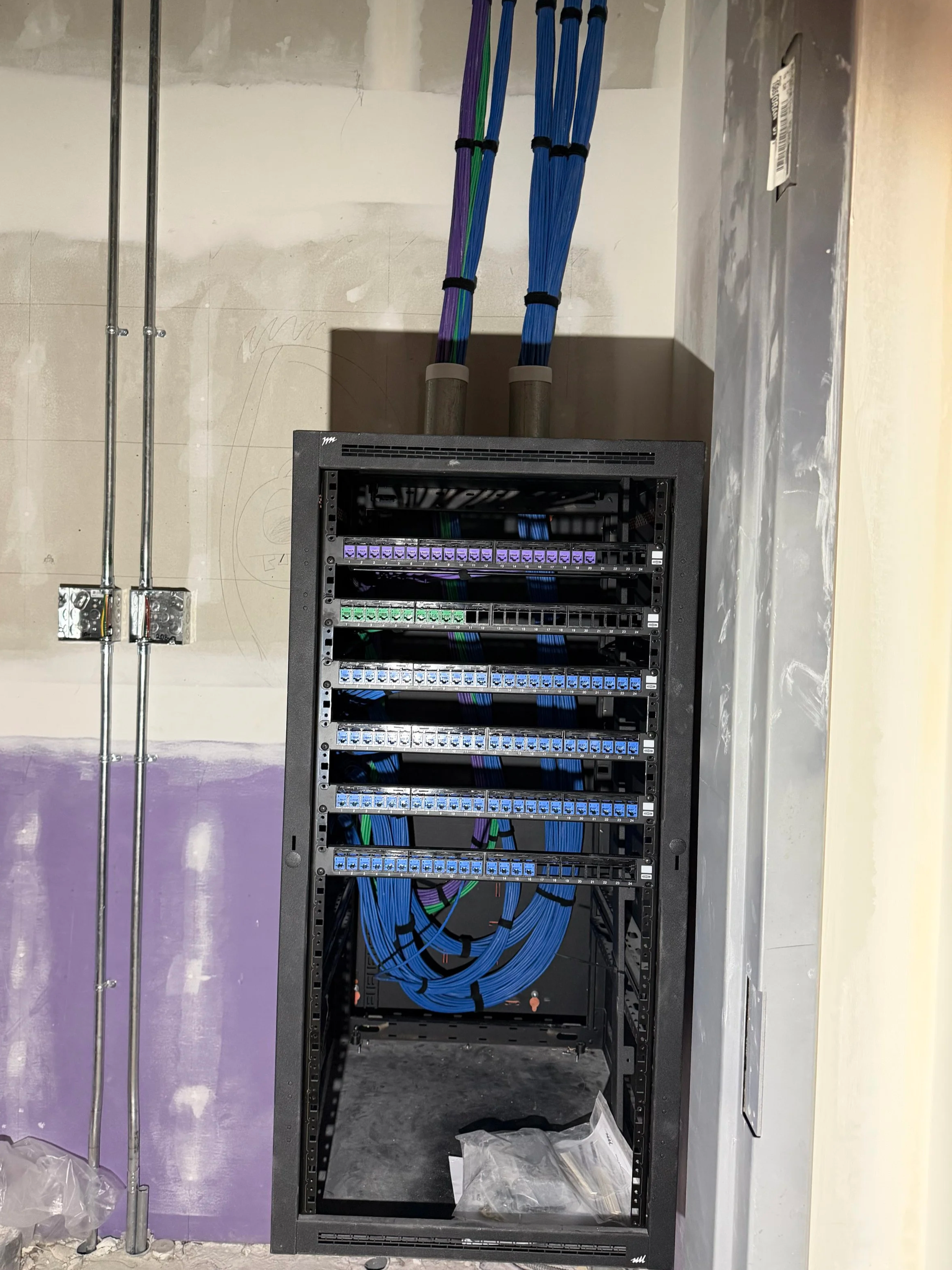 A black server rack with multiple blue, purple, green, and black network cables connected inside, with additional cables running through the ceiling.
Michigan structured cabling