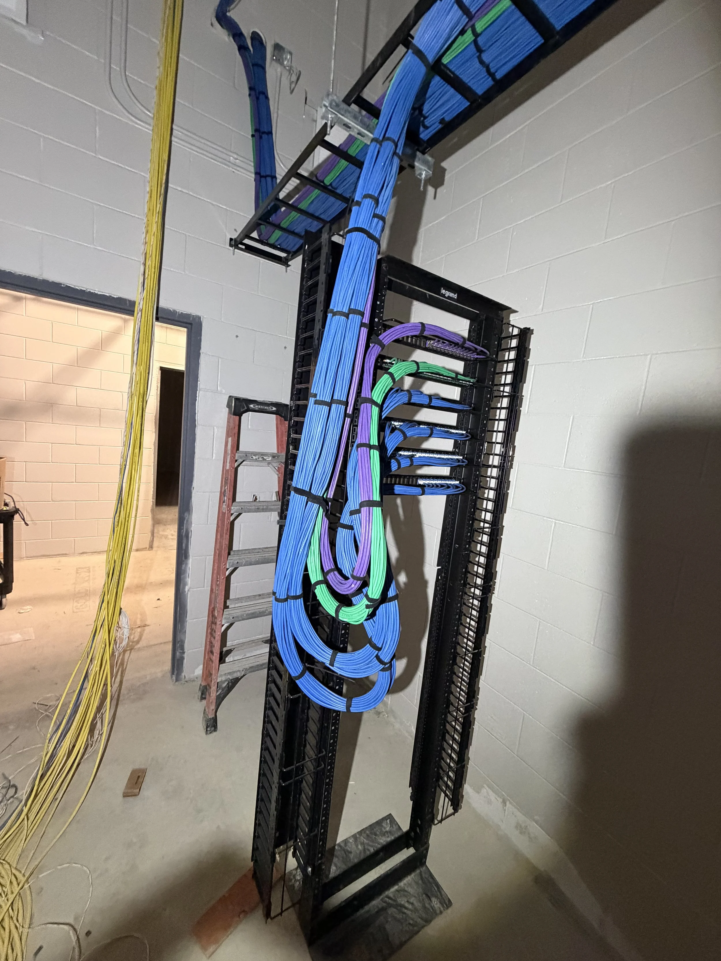 Colorful network cables organized in a server rack with a ladder nearby, inside a utility room with gray concrete blocks.
Michigan structured cabling