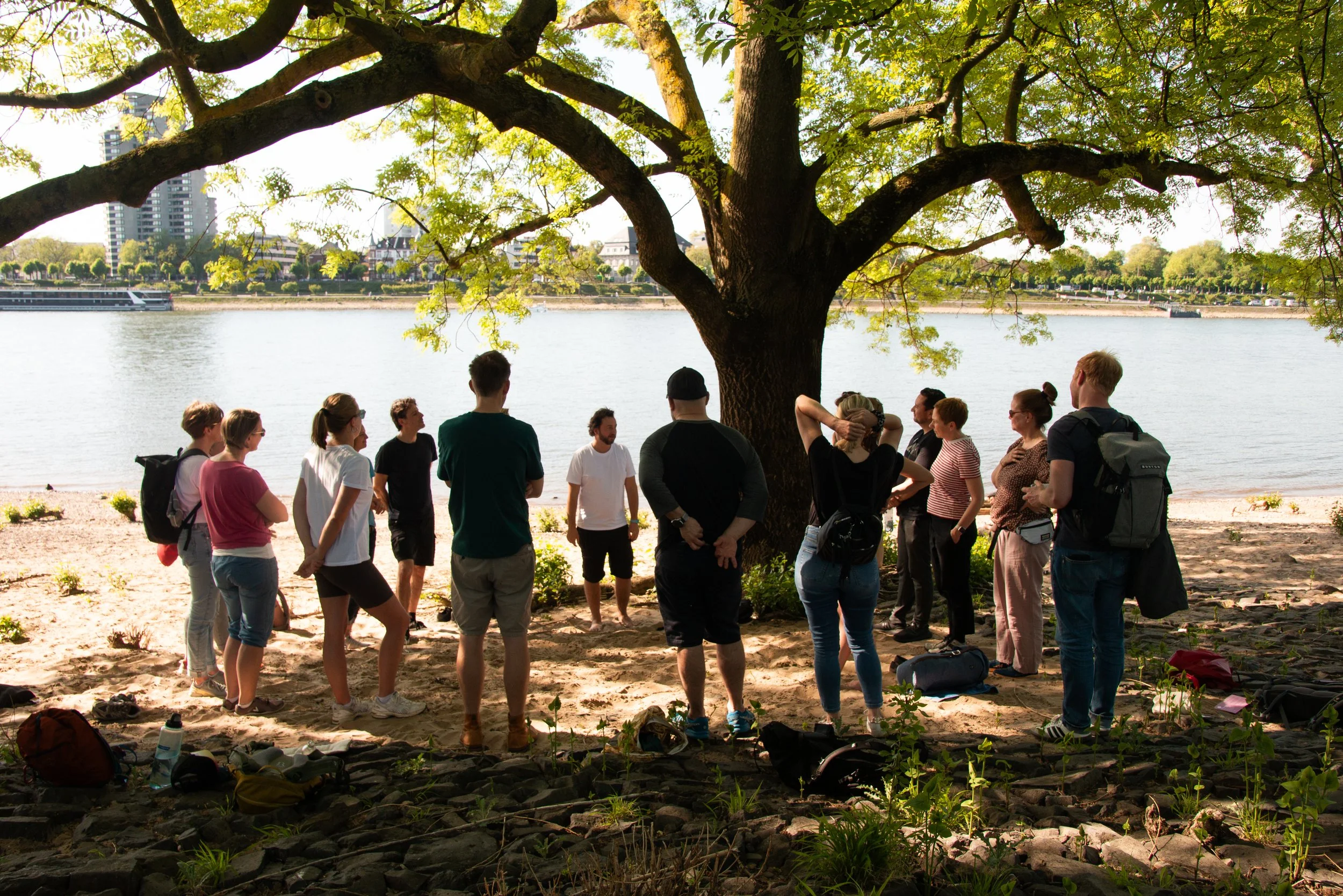Gruppe steht im Kreis unter einem Baum am Rheinufer bei einer Walkaboutyou-Übung in Köln