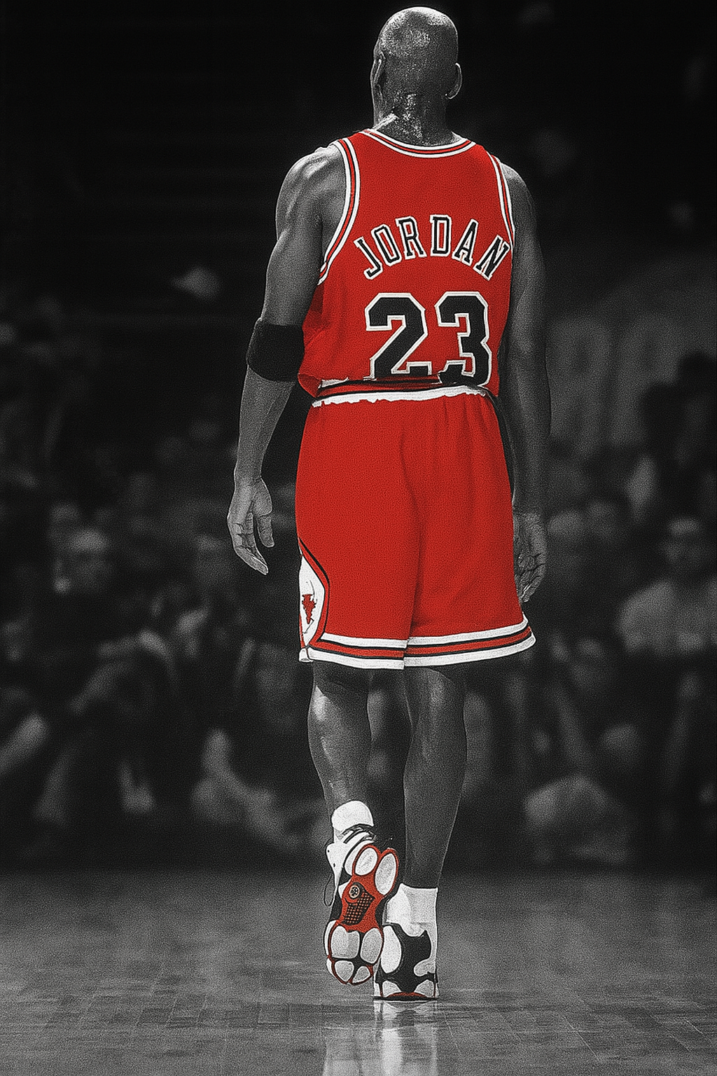 Back view of Michael Jordan wearing a red Chicago Bulls jersey with number 23 and his last name, walking on a basketball court with a blurred audience in the background.