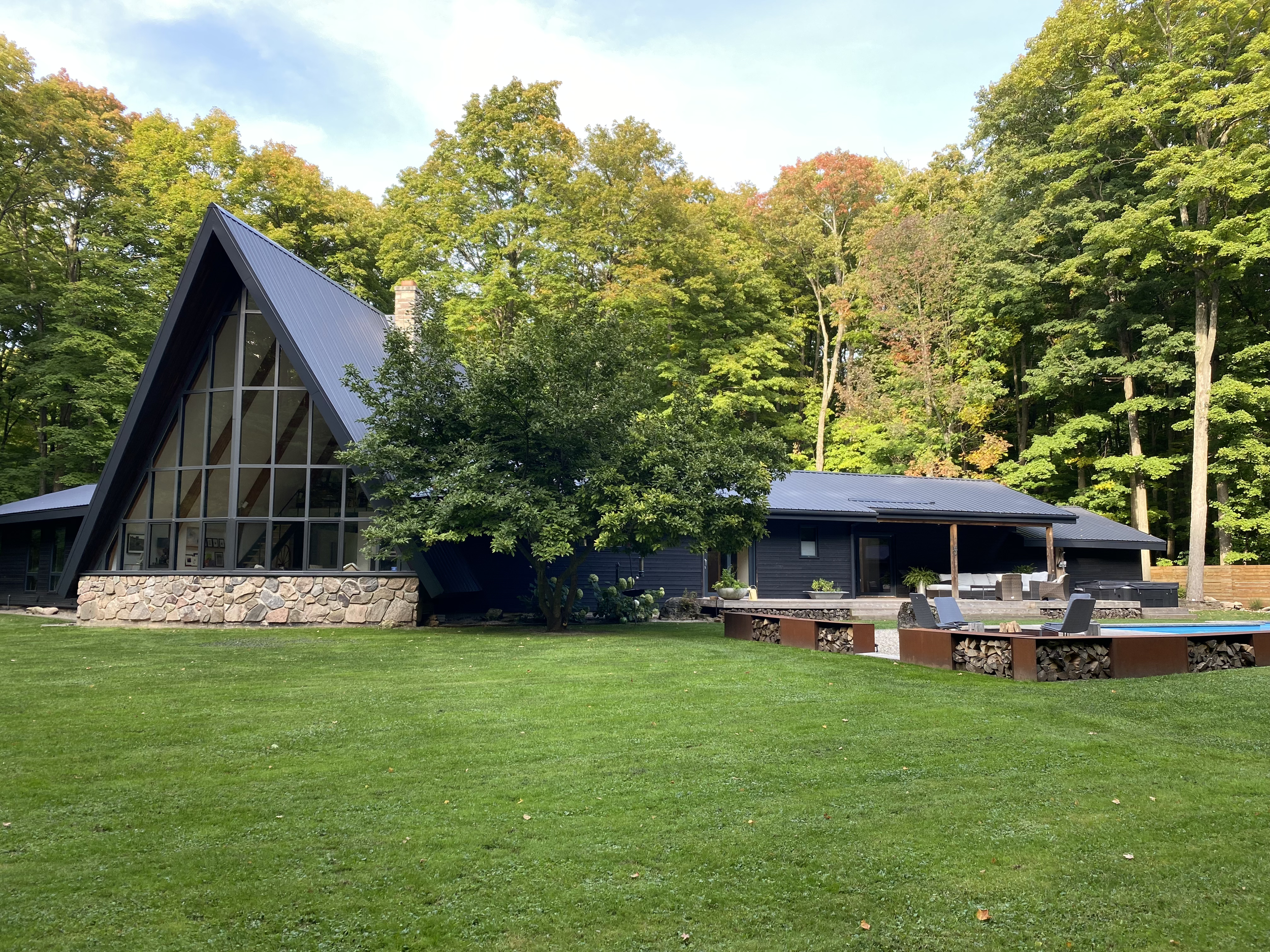 A-frame cabin with stone and glass facade surrounded by green lawn and trees