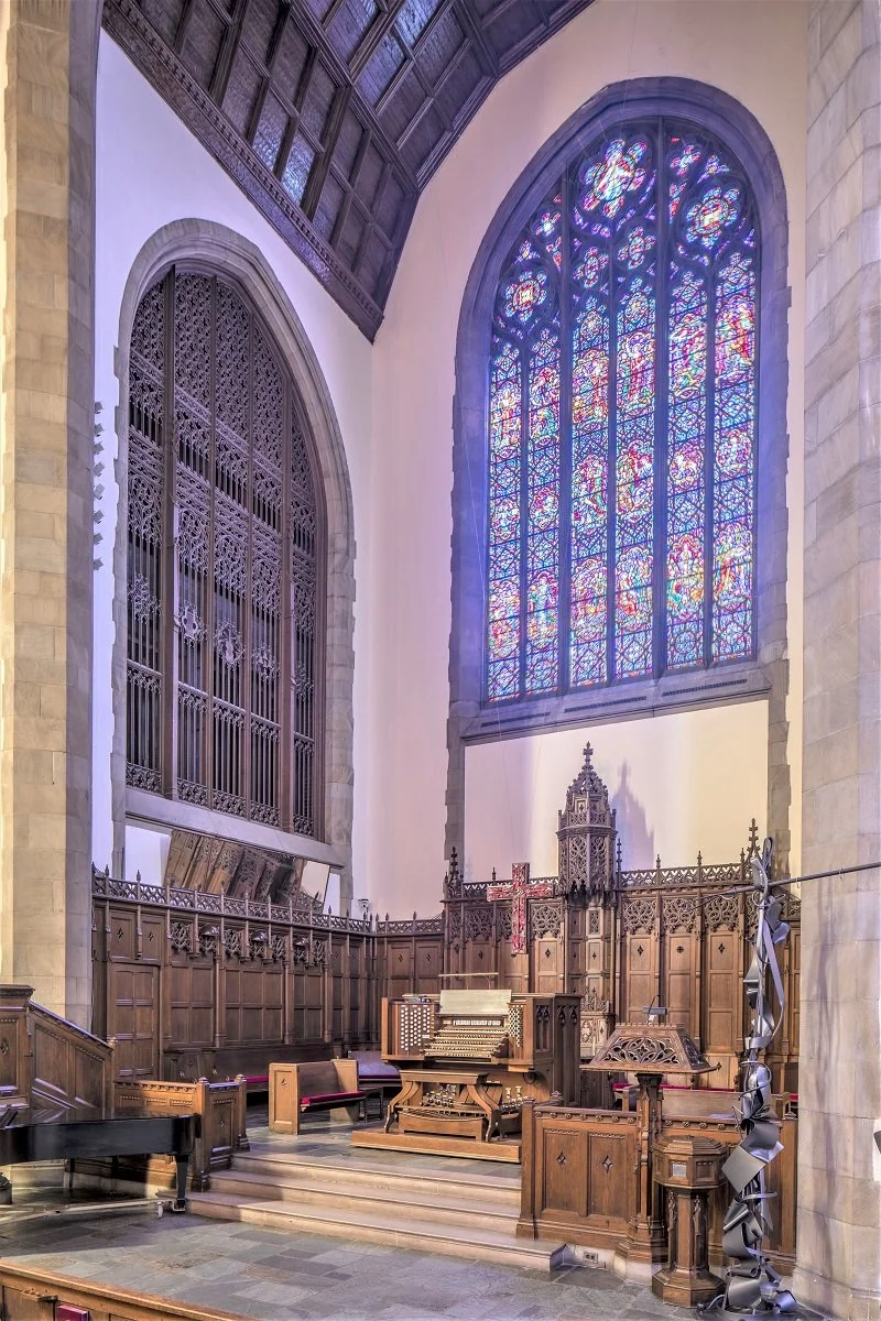 Interior of a church with stained glass windows, a pipe organ, and wooden choir stalls.