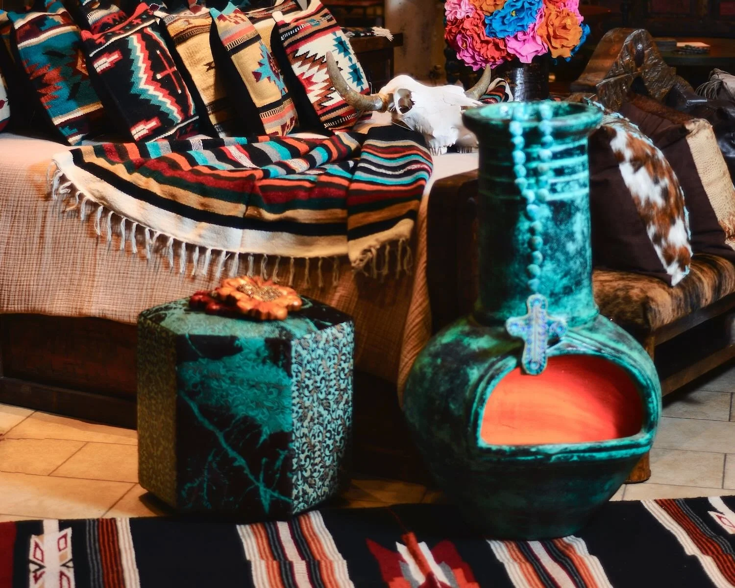 Turquoise clay chiminea, rosary beads and cowhide ottoman on a Southwest style rug in front of a handmade rustic bed from Mexico.