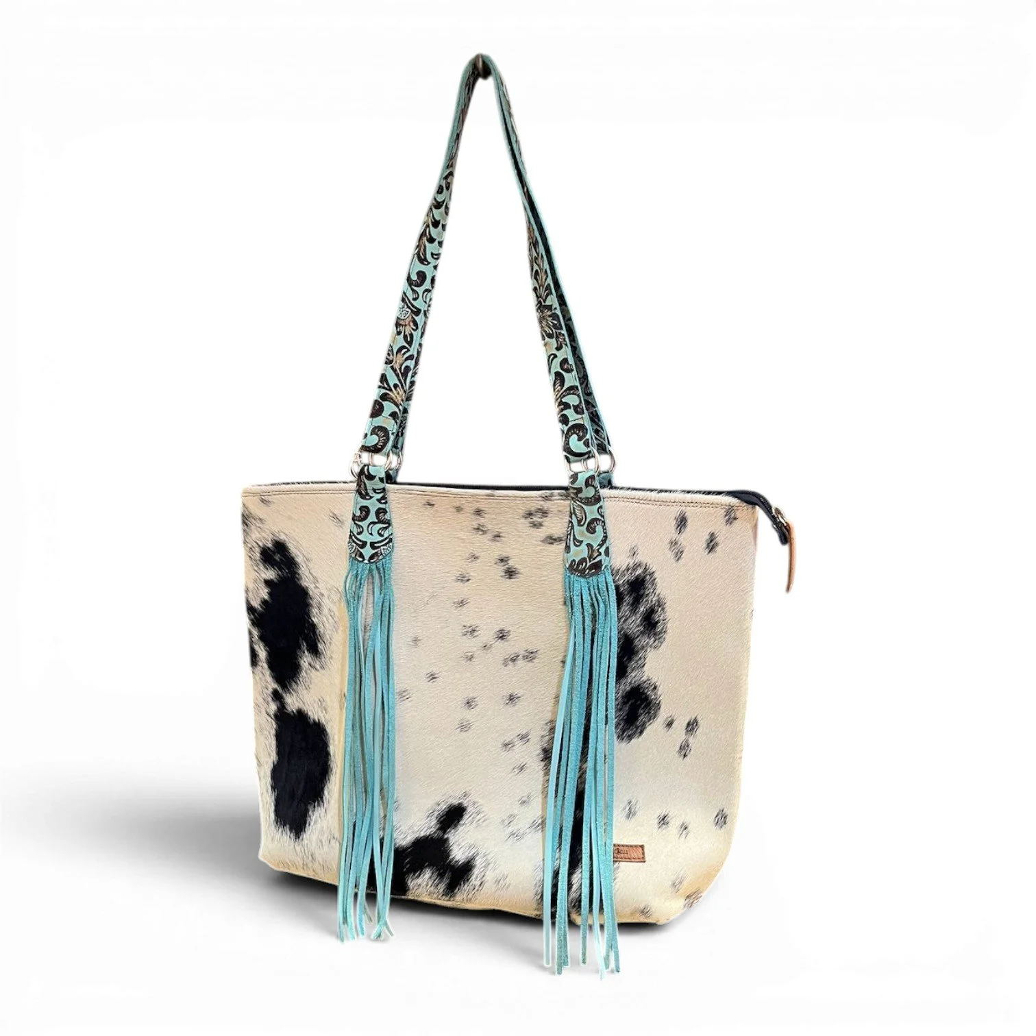 Handmade Brazilian Sheridan cowhide tote bag with black and white hide, black leather back, and turquoise fringe strap
