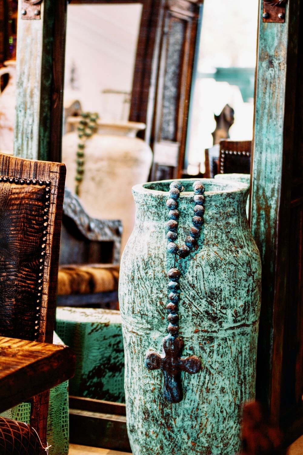 Handmade turquoise clay vase, rosary beads against a turquoise copper mirror from Mexico.