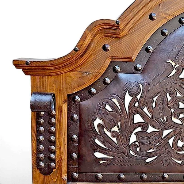 Handmade Arco de Herradura Western bed with arched headboard, tooled and perforated leather panels, carved wood, iron trim, and clavos.