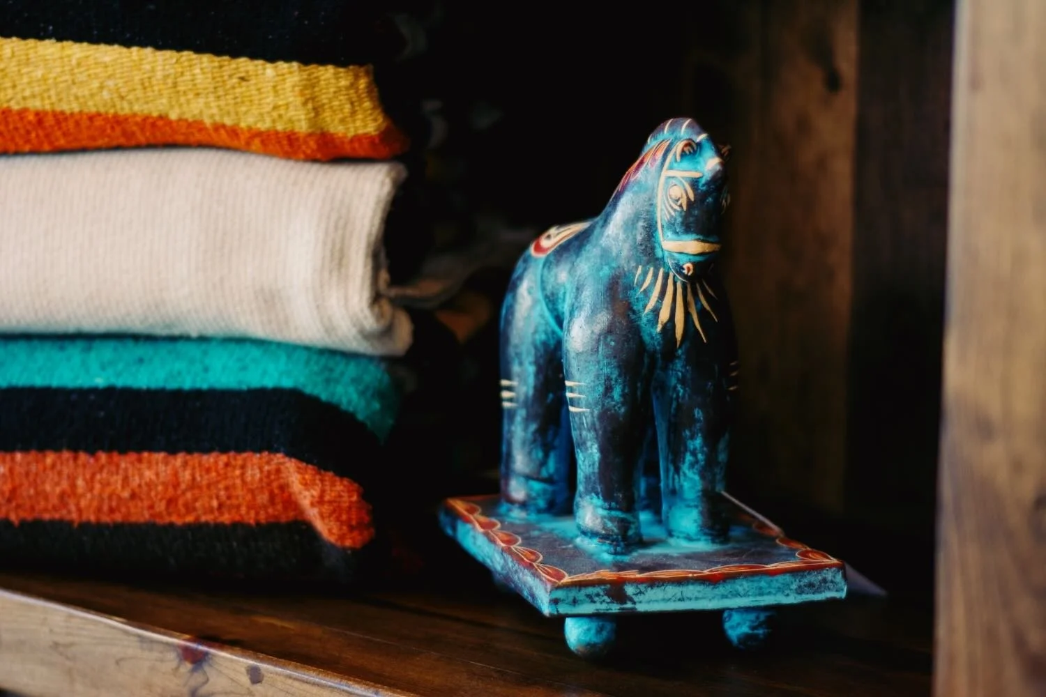 Handwoven mexican blankets with clay horse in a rustic curio cabinet.