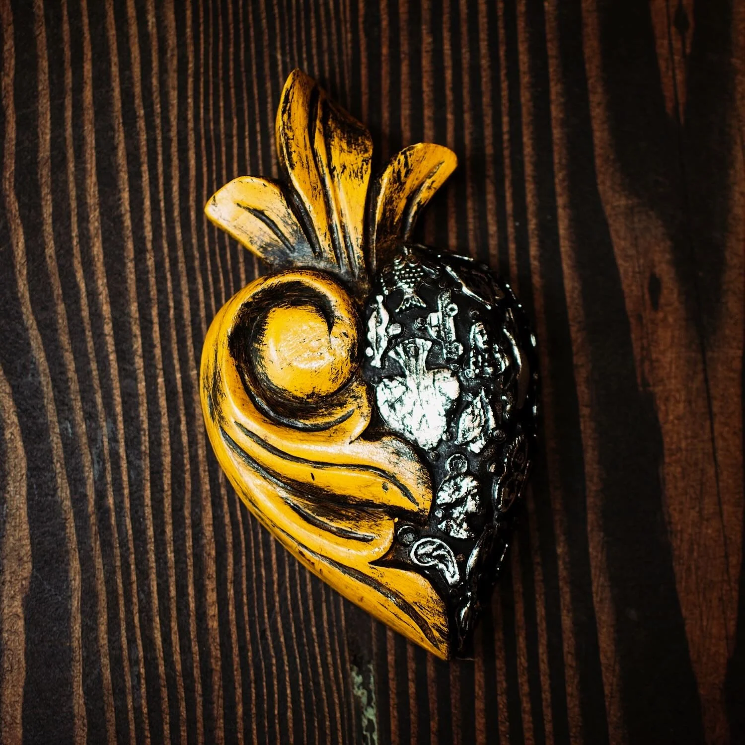Handmade Mexican yellow Milagros heart wall décor with a carved swirl design and traditional silver milagros charms.