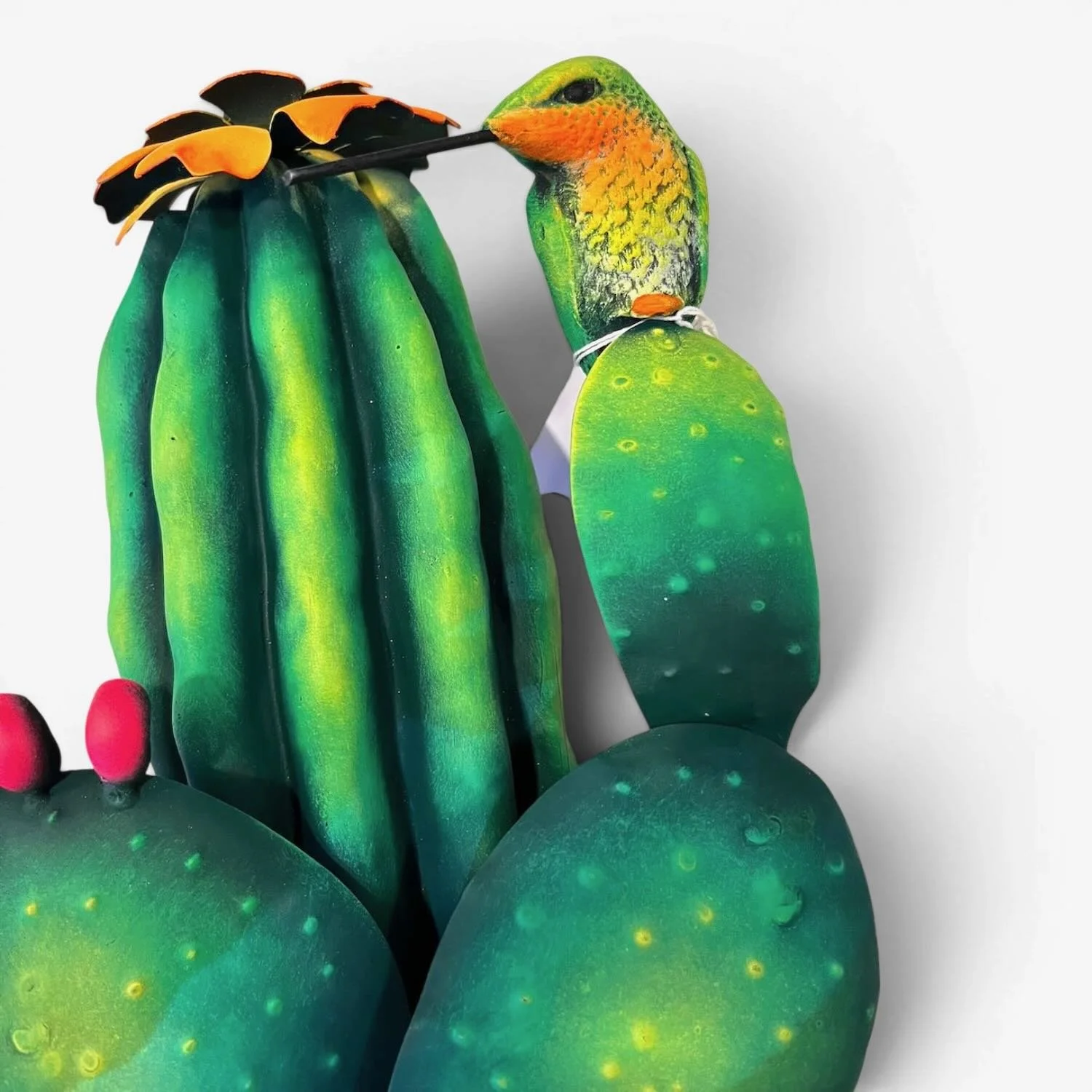 Handmade Mexican metal wall art featuring a colorful hummingbird perched on a prickly pear cactus with a saguaro cactus in the background.