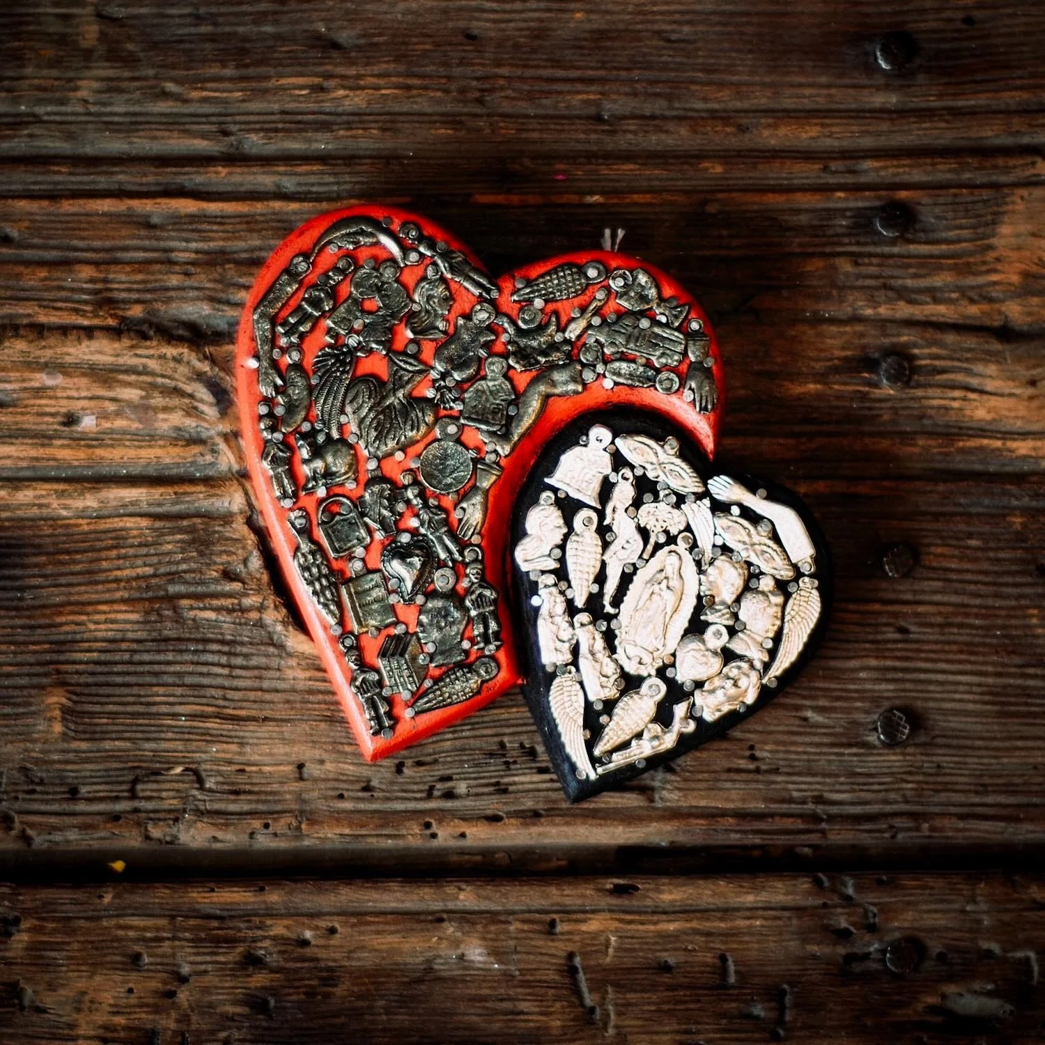 Handmade Mexican double heart wall décor with red and black hand-painted hearts accented by traditional silver Milagros charms.