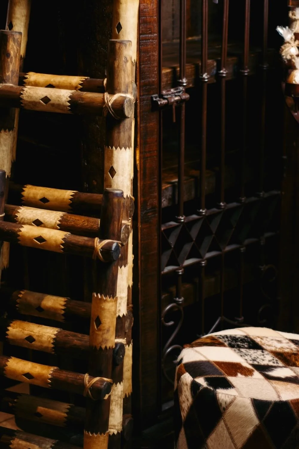 Reclaimed wood ladders wrapped in rawhide leather, a cowhide ottoman and large rustic curio cabinet with iron doors.