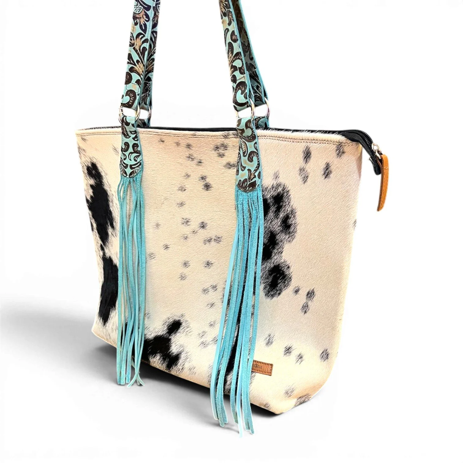 Handmade Brazilian Sheridan cowhide tote bag with black and white hide, black leather back, and turquoise fringe strap