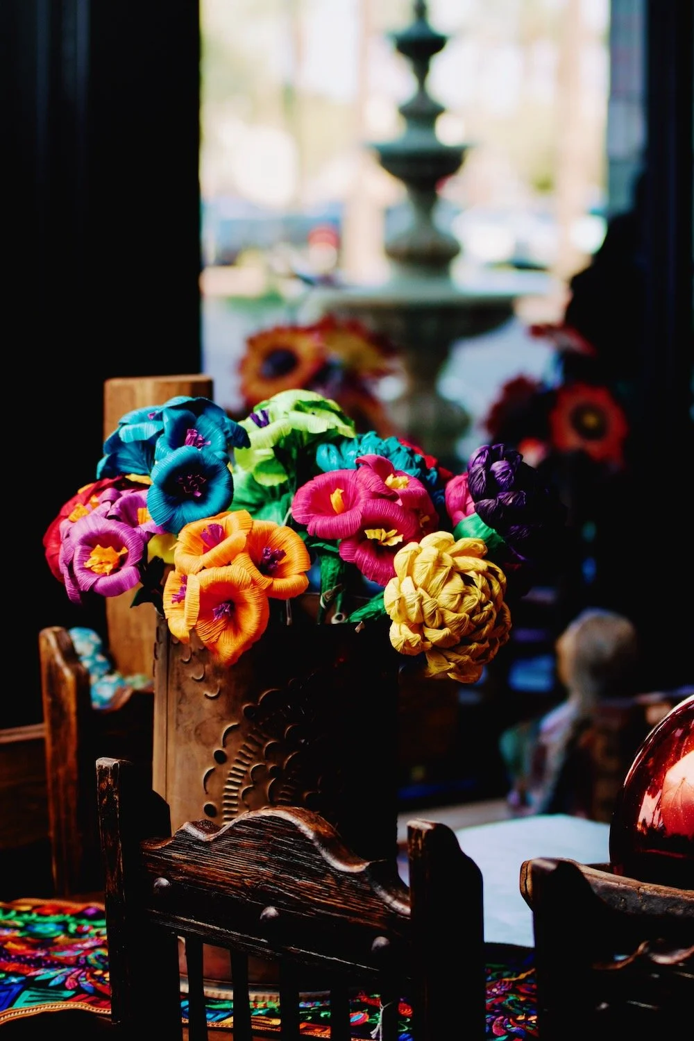 Colorful handmade cornhusk flowers in a bronze luminaria overlooking the fountain at Village Square at Dana Park. Visit the Milagros Rústicos showroom.