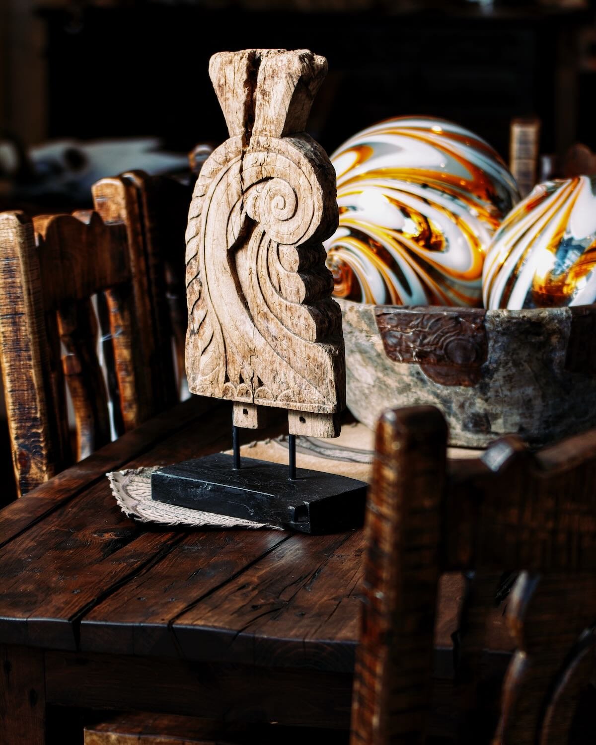 Unique carved table art on a rustic dining table from Mexico. Handblown glass spheres in a distressed antique wood bowl in the background.