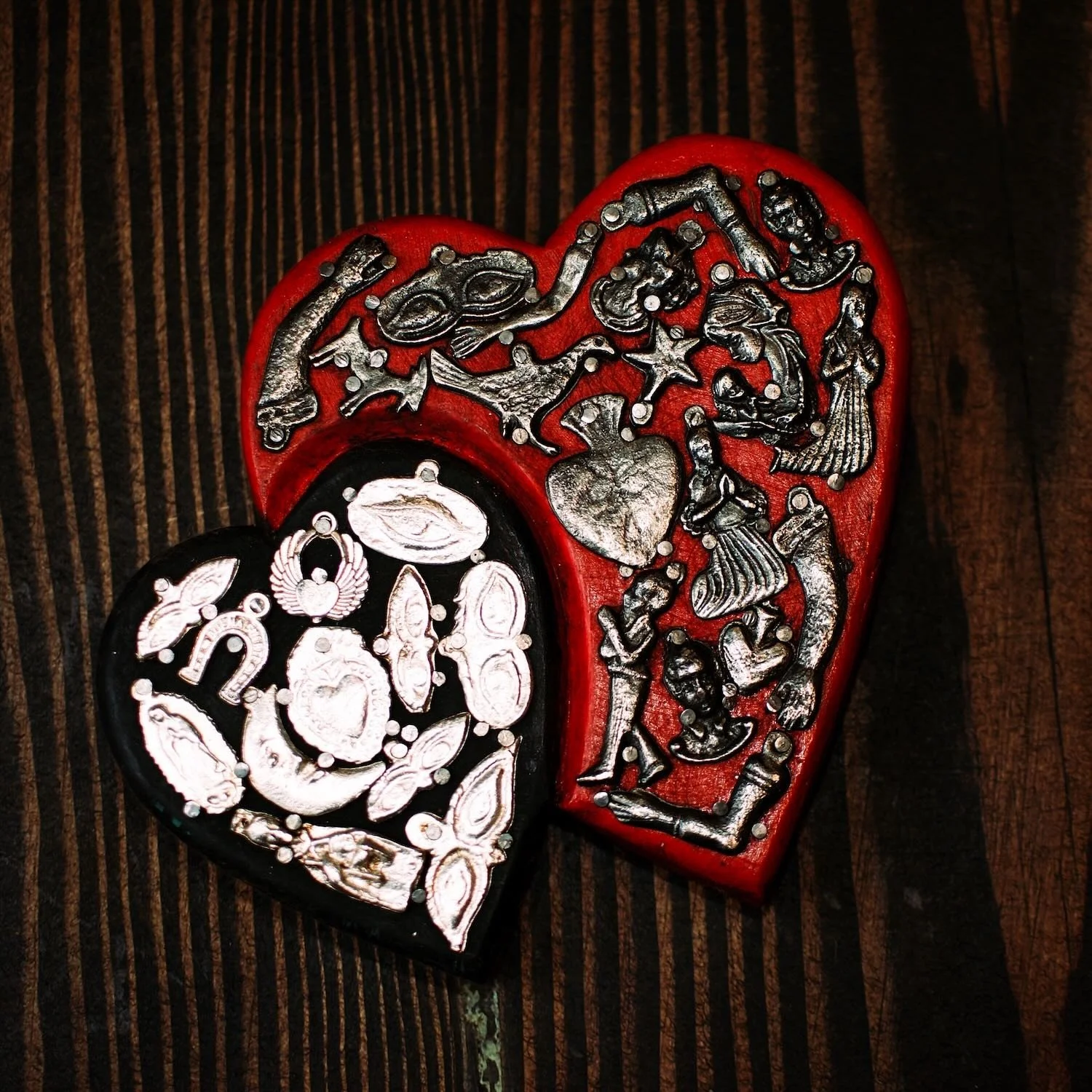 Handmade Mexican double heart wall décor with red and black hand-painted hearts accented by traditional silver Milagros charms.