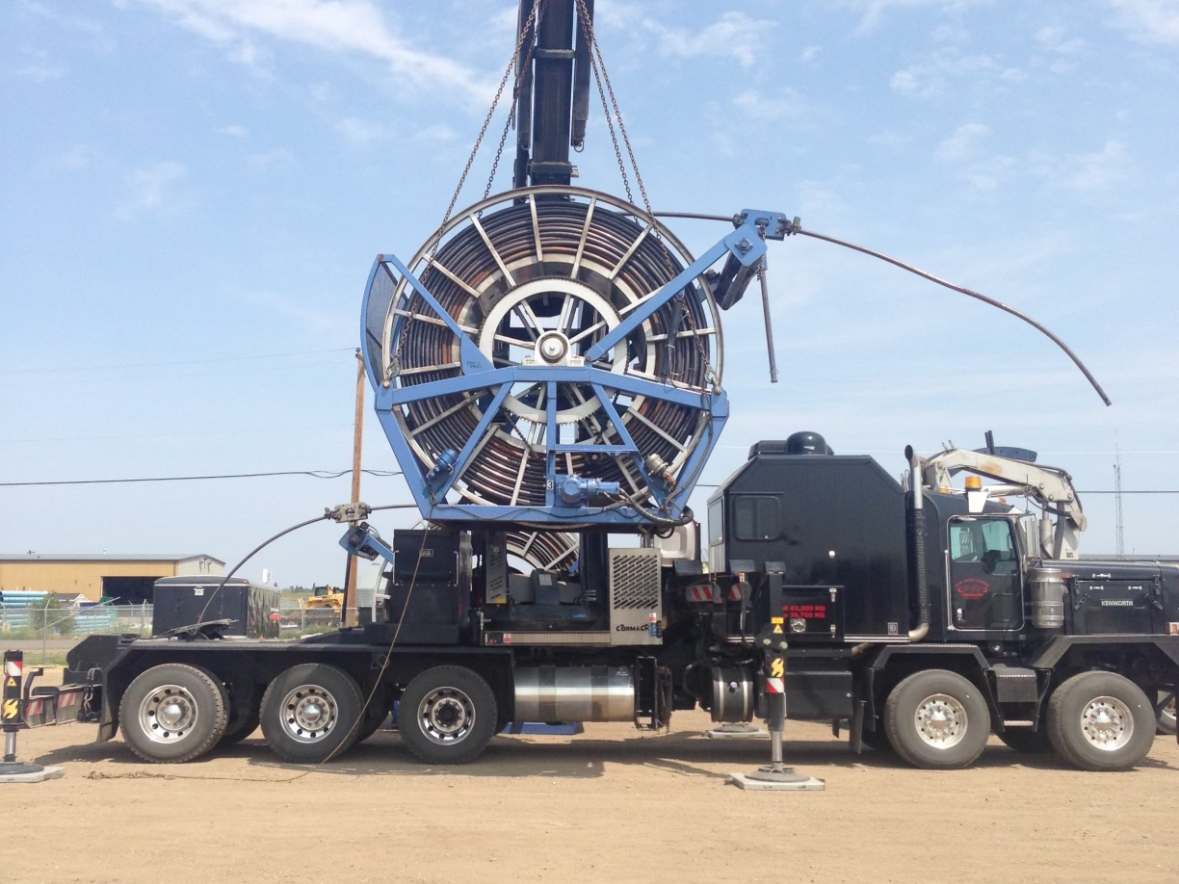 Large industrial machine mounted on a black truck with eight wheels, positioned on a dirt surface, under a mostly clear blue sky.