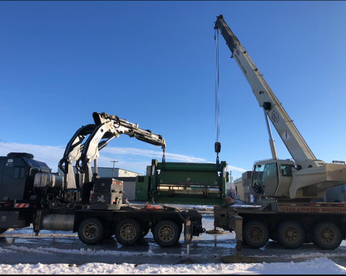 Two large cranes lifting a green object outdoors in snowy weather with clear blue skies.