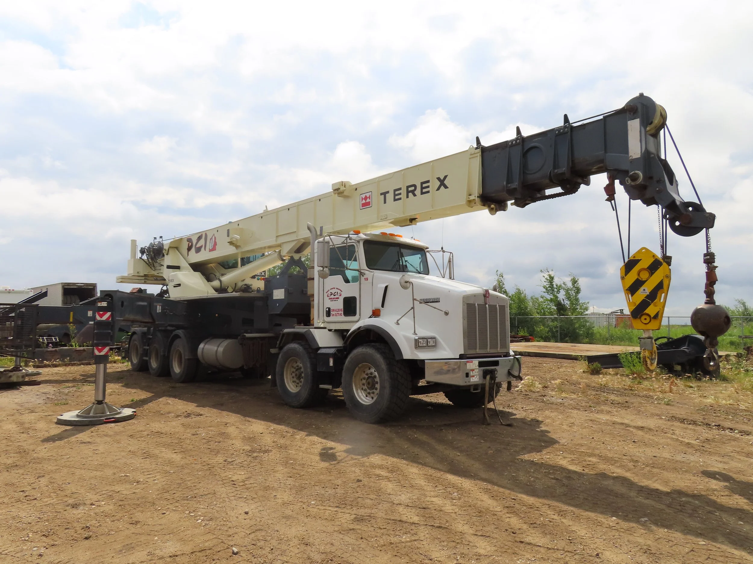 A white crane truck with the brand name 'TEREX' and 'PCI' on the boom, parked on a dirt surface under a cloudy sky.