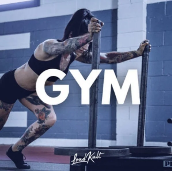 Mujer con tattoos haciendo ejercicio en el gimnasio con una barra de pesas.