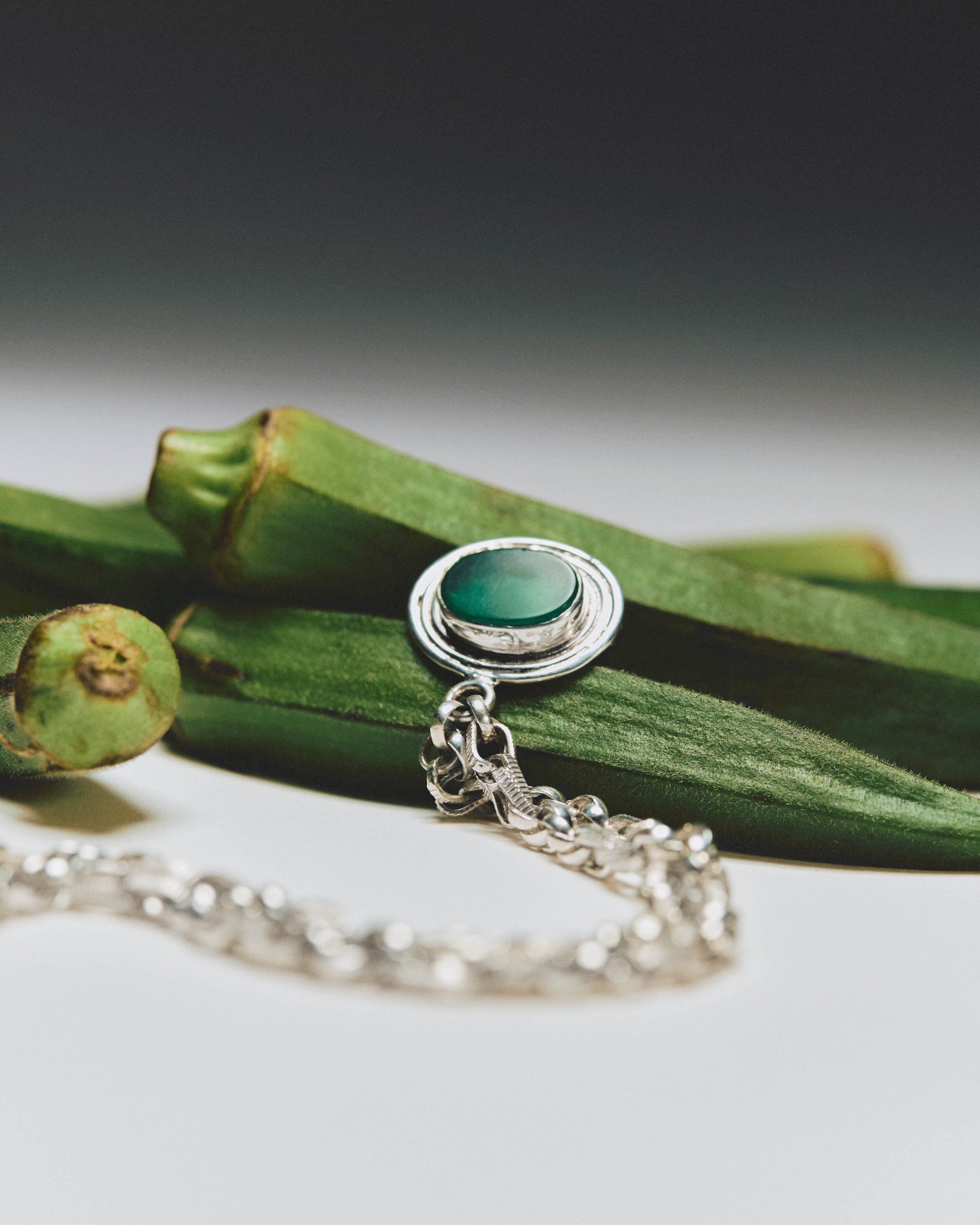 Silver necklace with a green stone pendant on green vegetable background