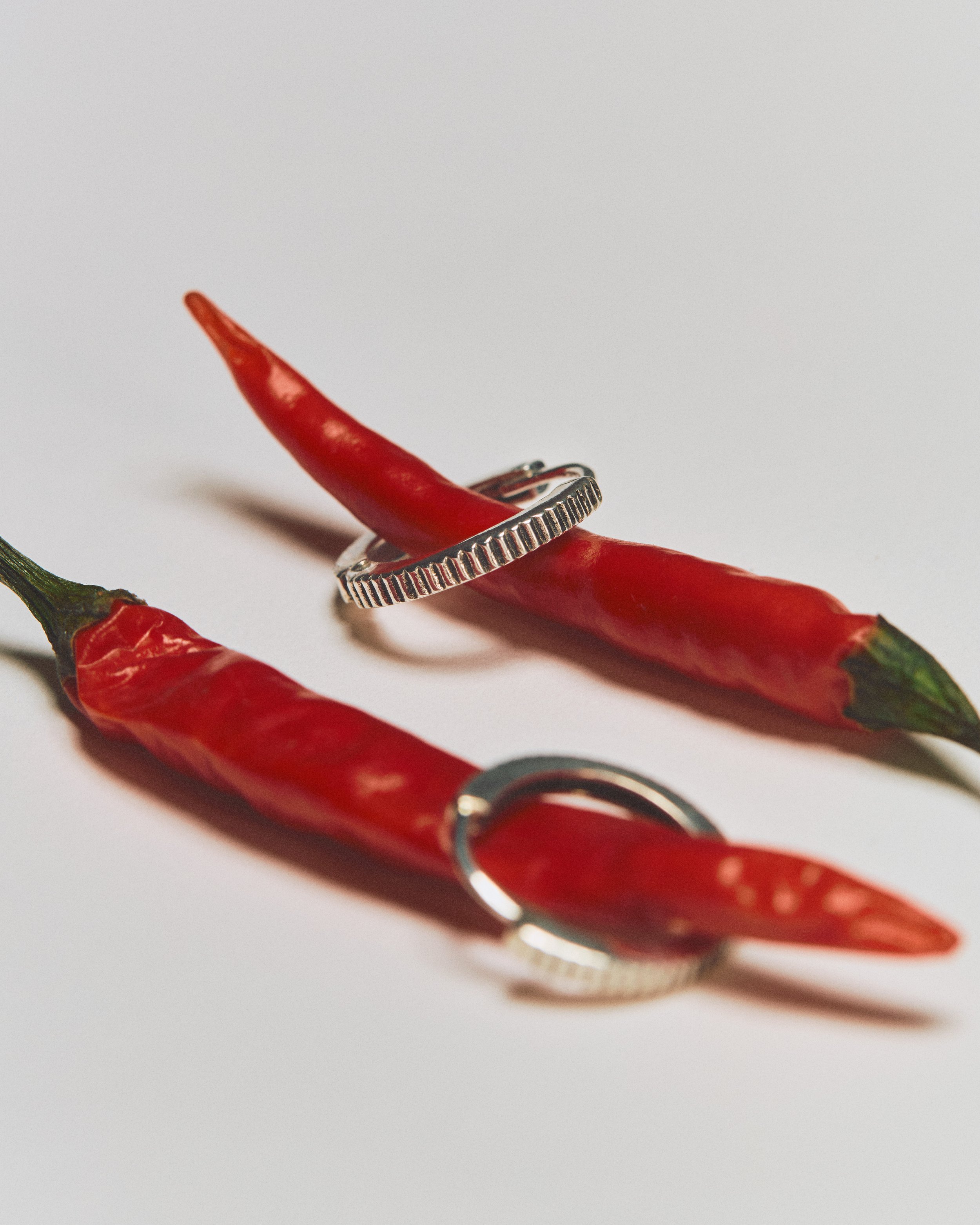 Two red chili peppers with silver rings encircling them on a white background.