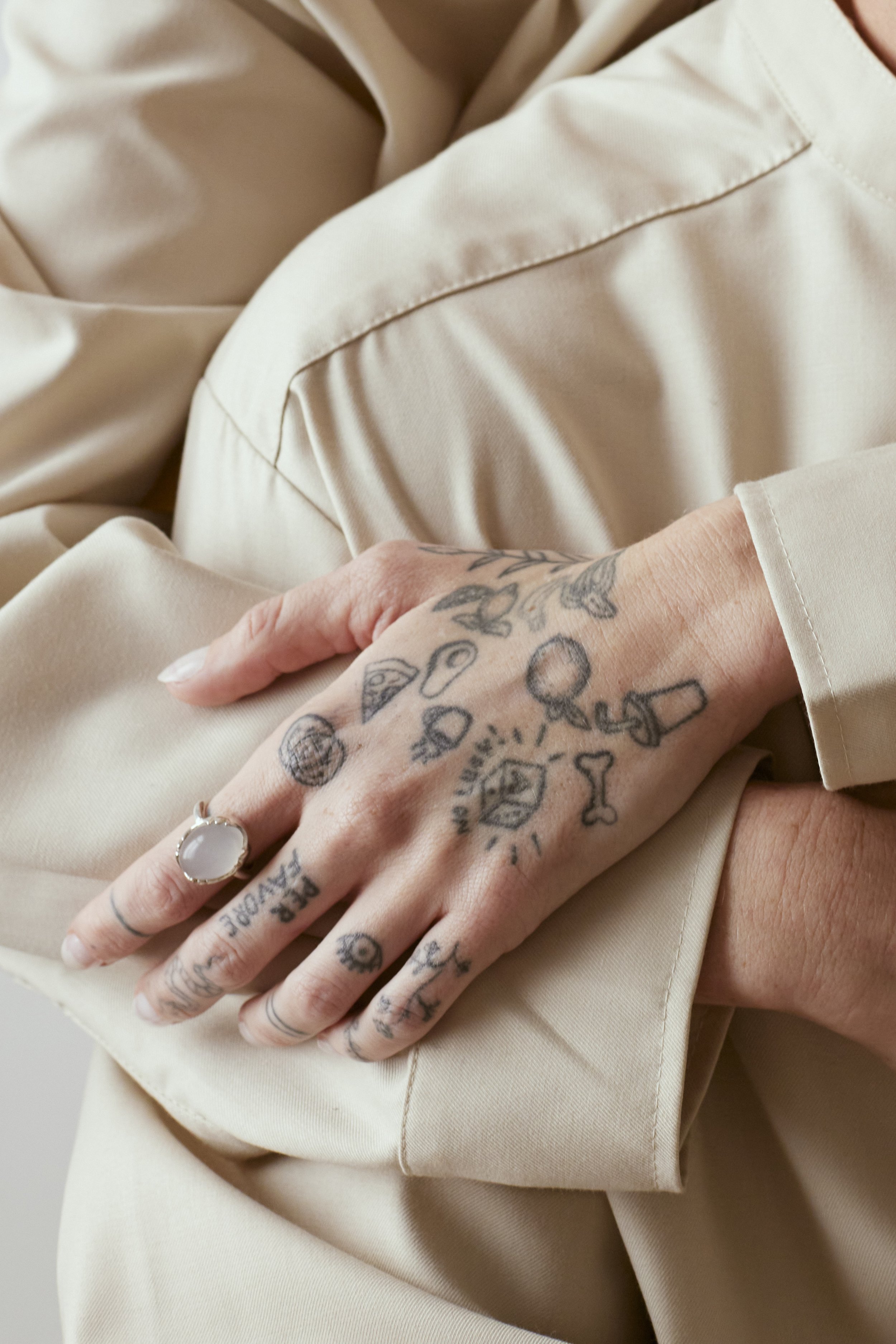 Close-up of a tattooed hand with a ring, resting on beige fabric.