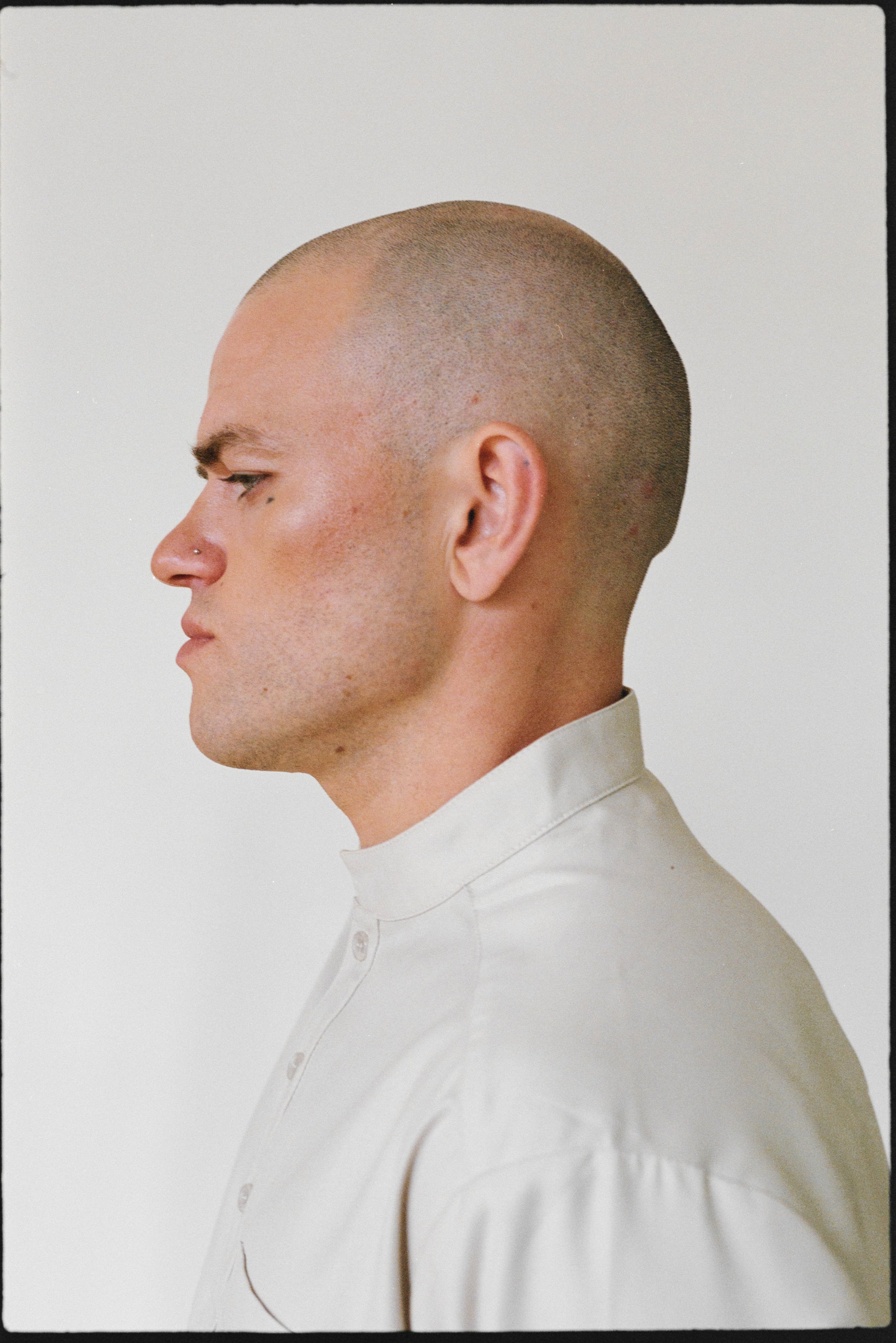 Profile of a bald person wearing a light-colored button-up shirt against a plain background.