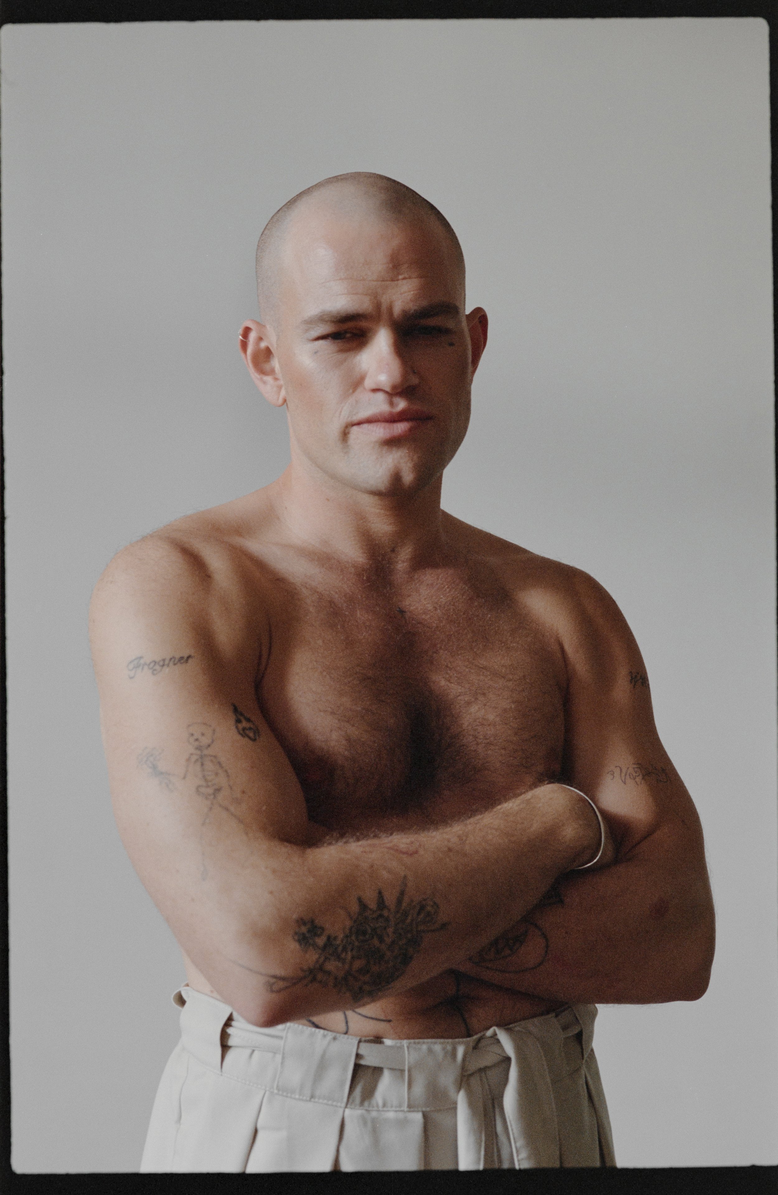 Shirtless man with tattoos, arms crossed, neutral expression