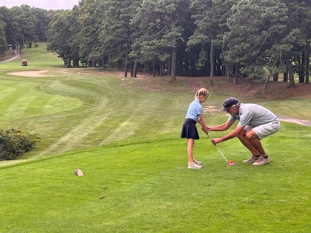 Adult teaching child how to golf on a grassy course