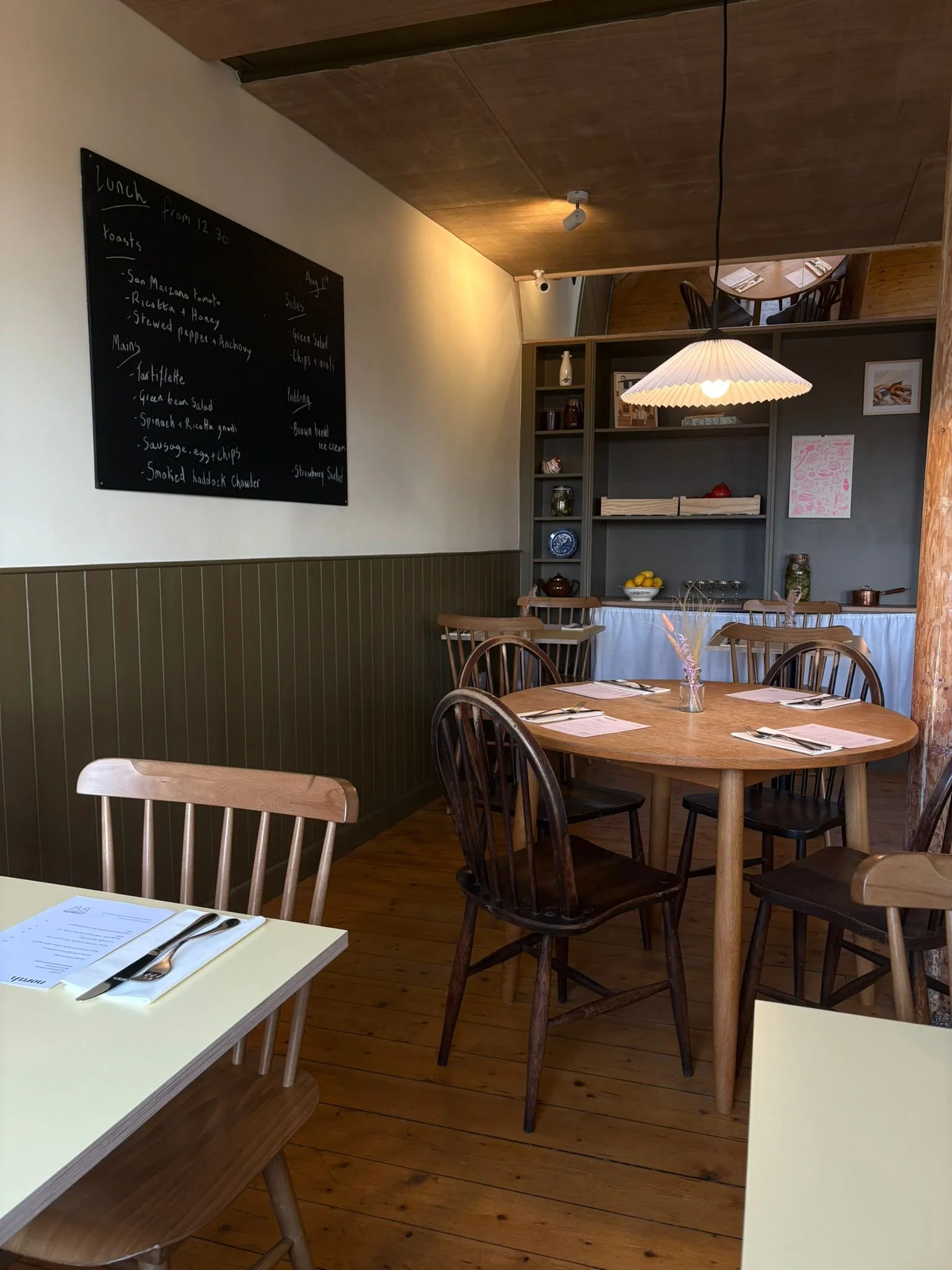 Cozy restaurant interior with wooden tables and chairs, a chalkboard menu on the wall, and a white pendant lamp lighting the space.