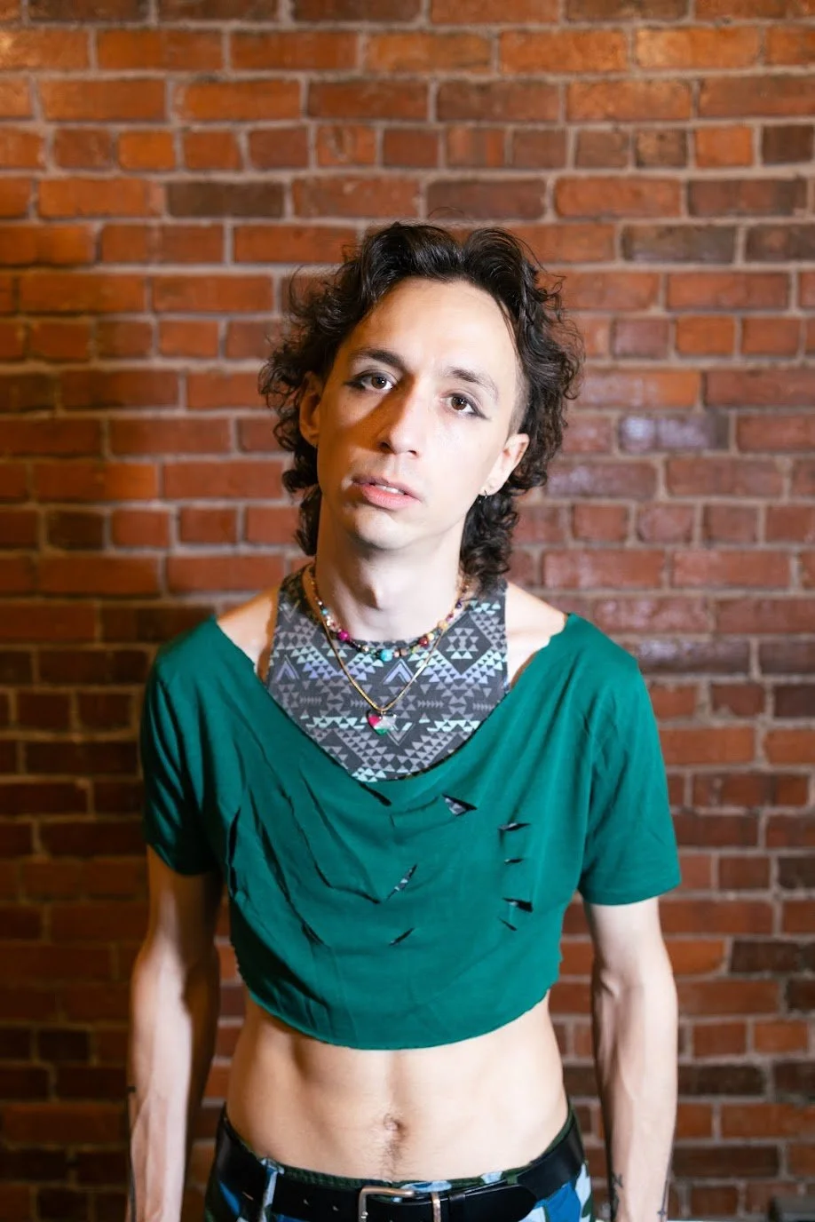 Man staring at the camera, He has brown curly hair, he is wearing a green shirt