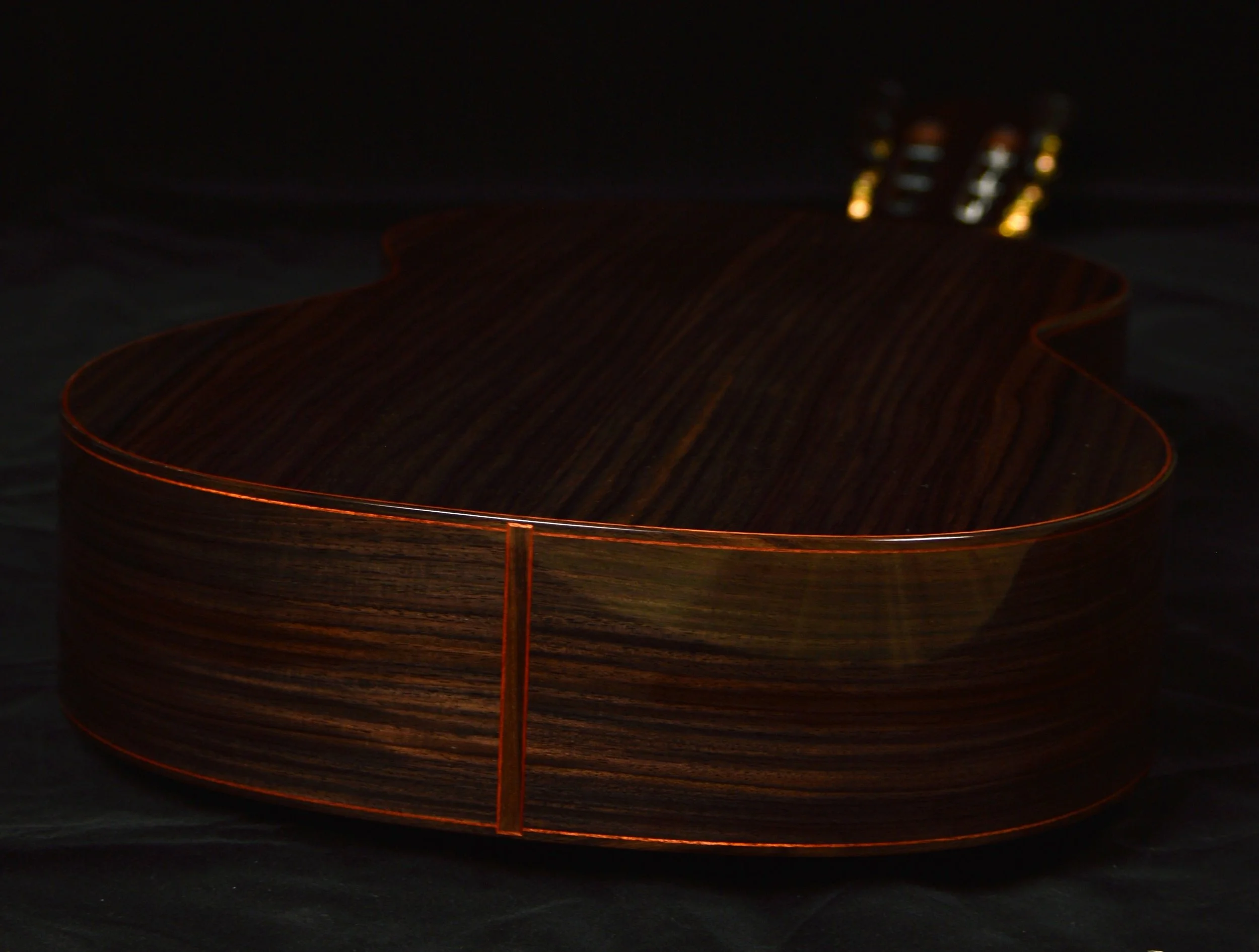 Close up of the rosewood and bloodwood end graft on a classical guitar on a black background.