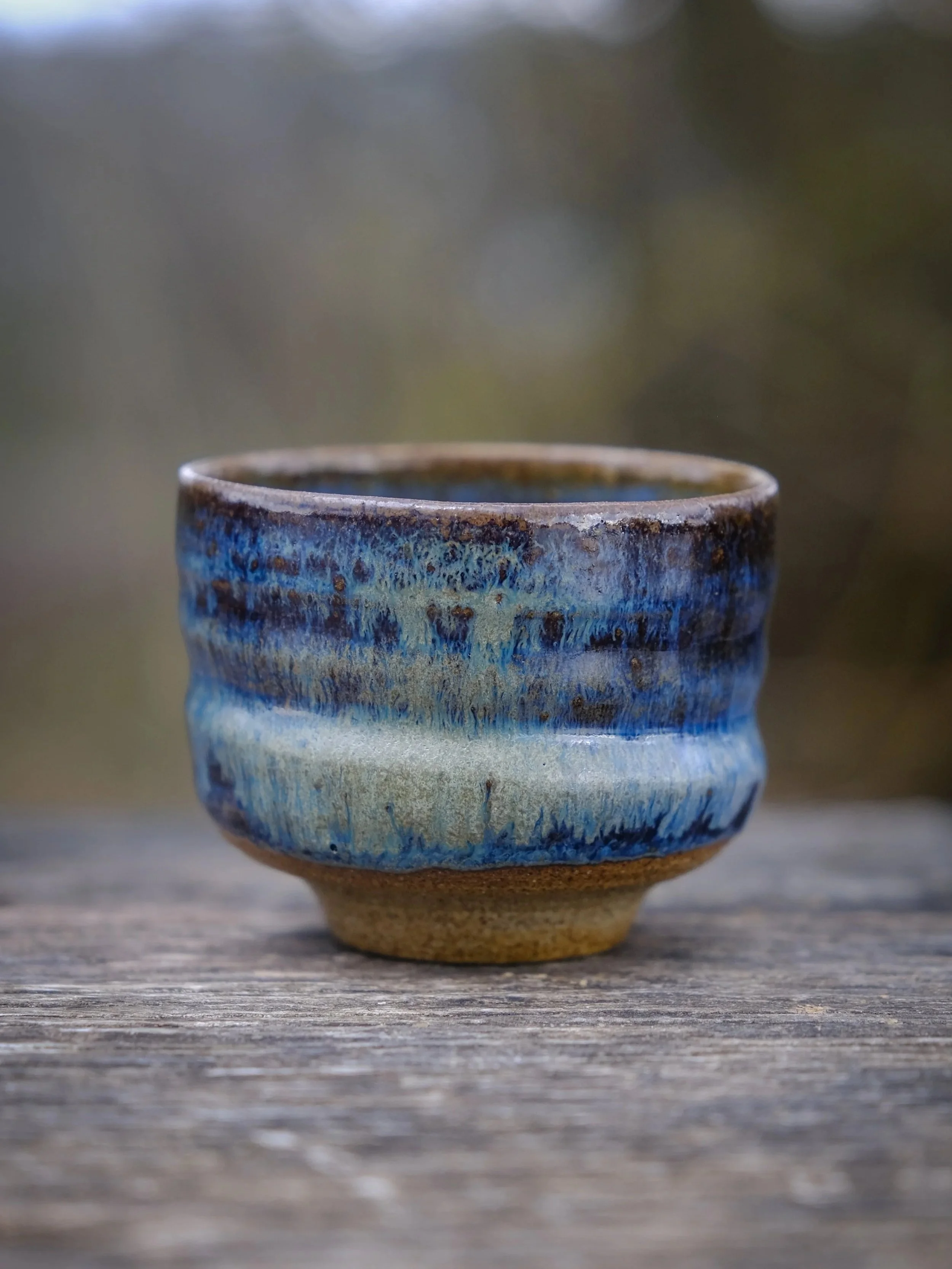 A close-up of a wabi-sabi organic cup in natural raw clay and watter-like blue finish.