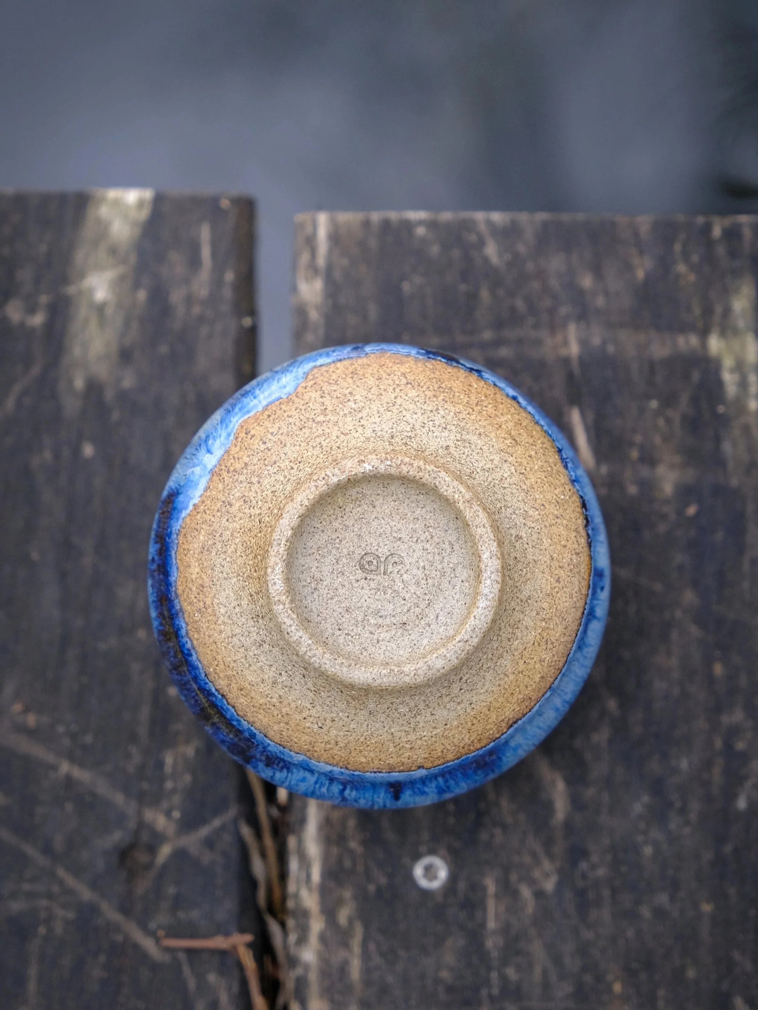 Stone-like, earthy, unglazed, natural bottom of the cup featuring the makers signature.