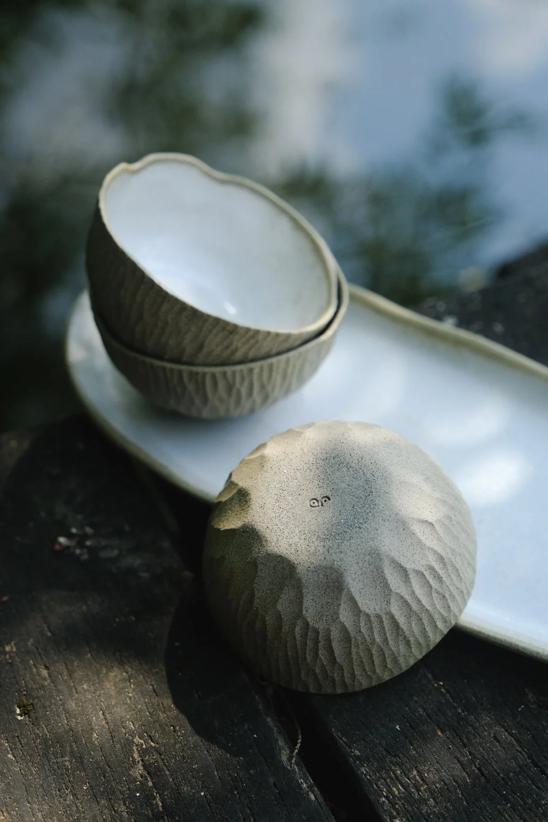 Close-up of the hand-textured raw stone-like bowls and a plate finished with rustic off-white glaze.