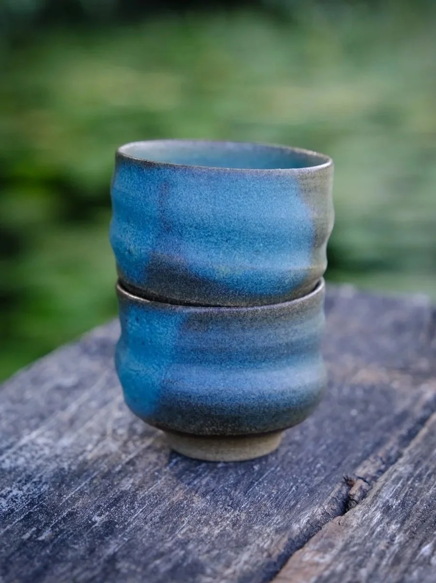 Handmade swirly wabi-sabi cups stacked in a natural setting.