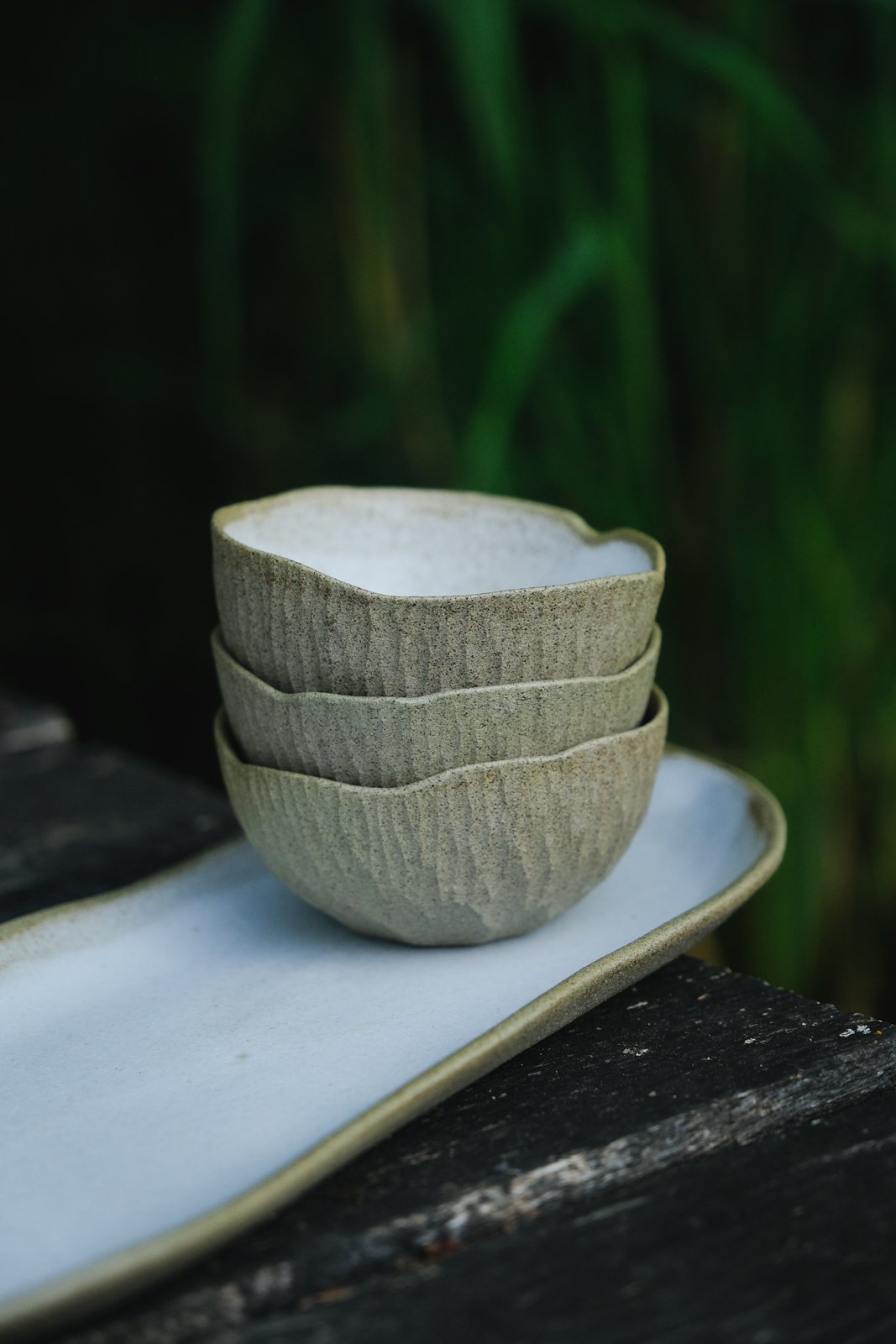 Petite Earth bowls stacked on an elongated tray with hand-carved texture and rustic white surface visible.