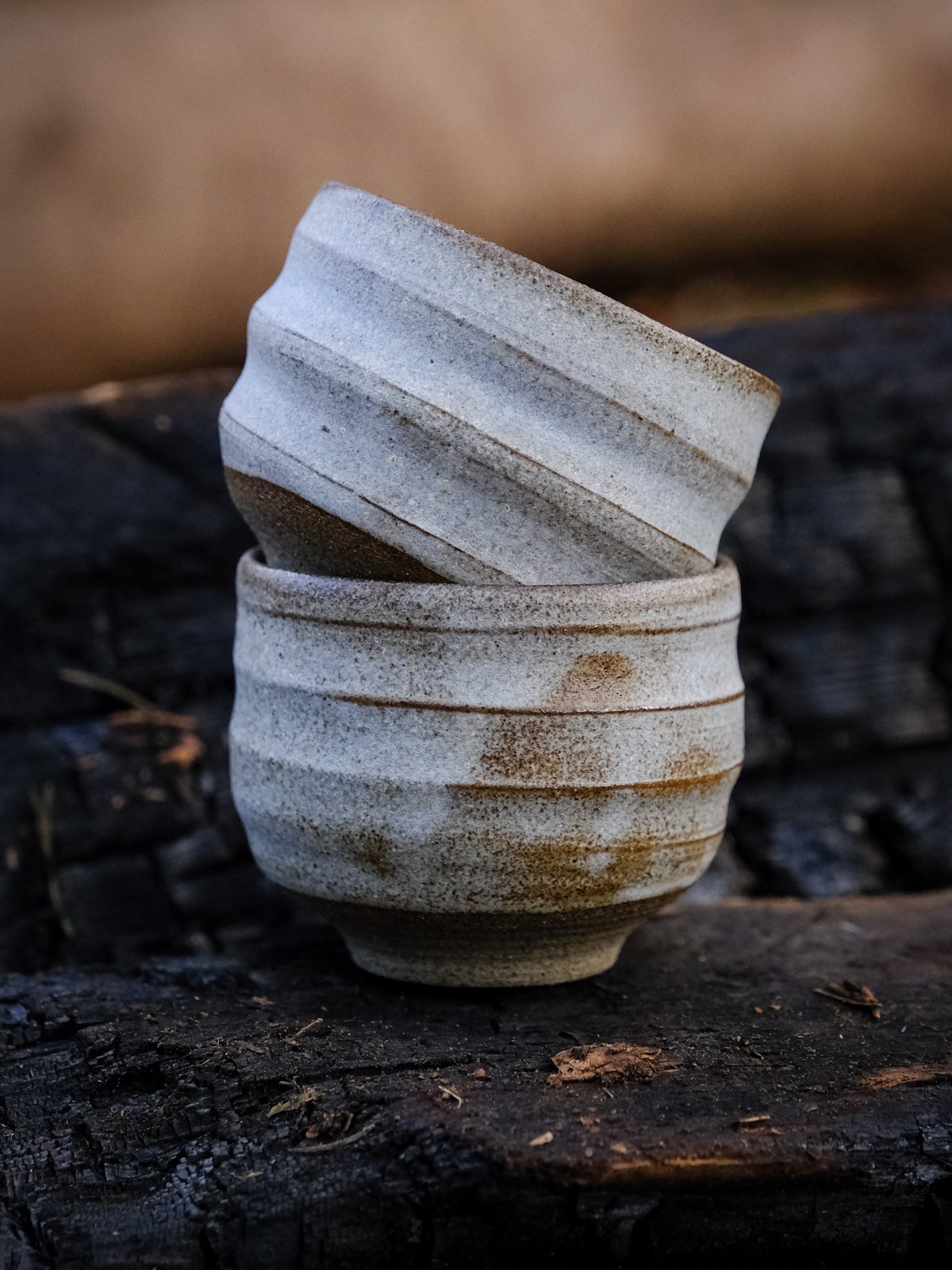 A pair of natural wabi-sabi cups stacked and featuring a swirly organic form.