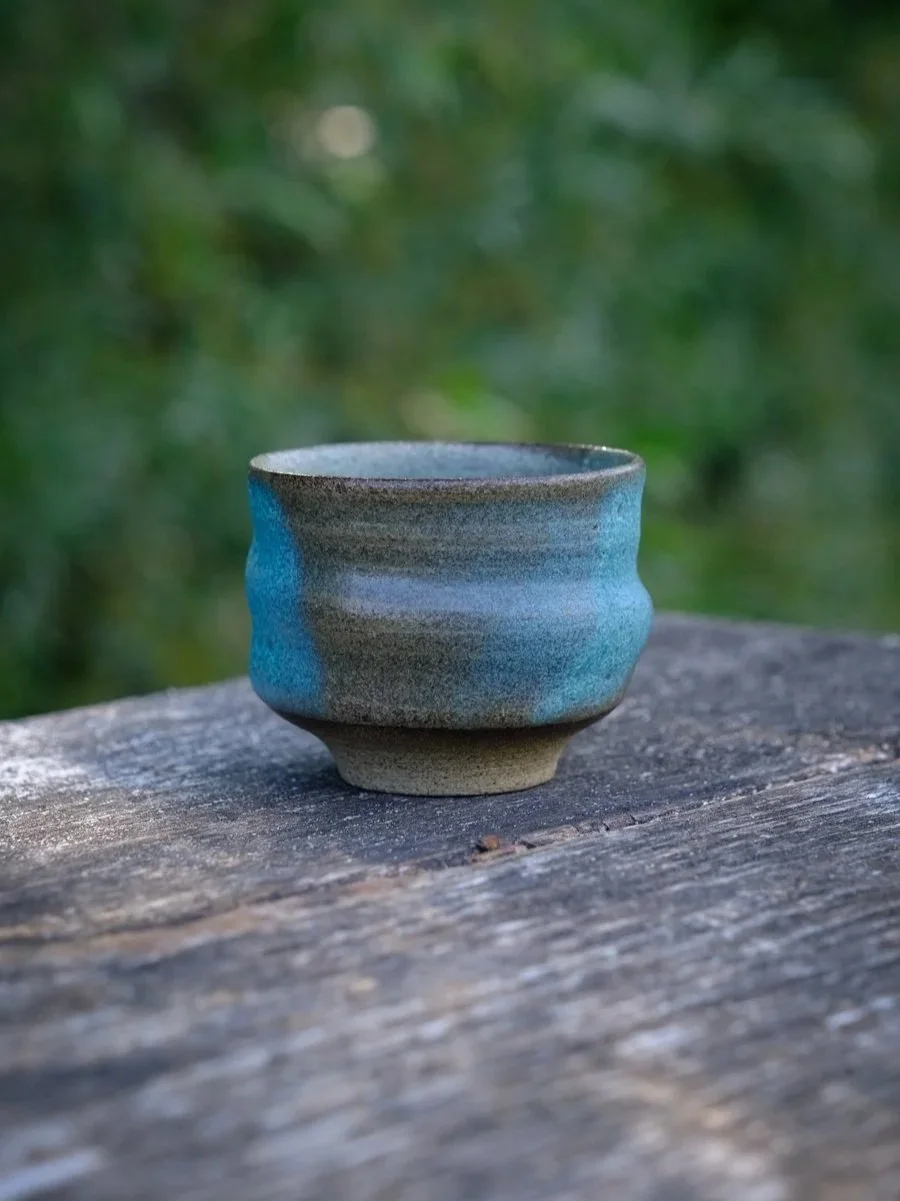 A side view of a undulating swirly cup in green matte finish with soft brown efects.