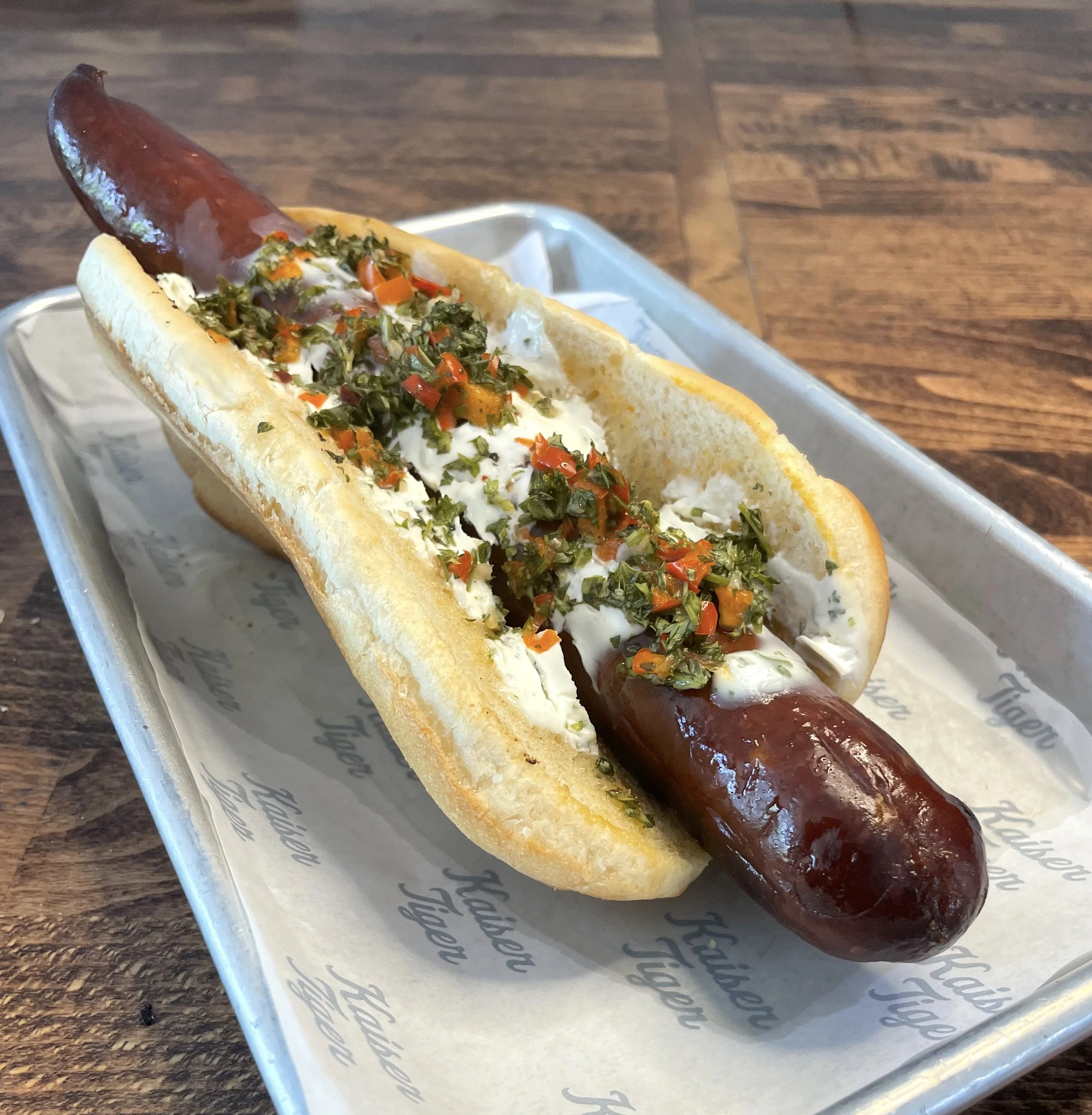 Gourmet sausage sandwich with toppings on a tray.