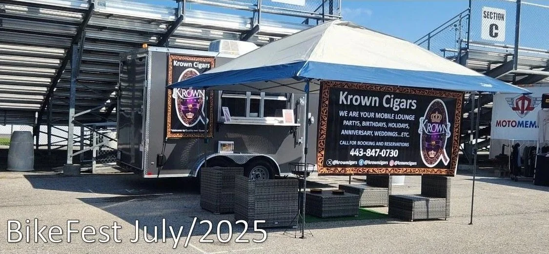 A small trailer with a canopy set up as a lounge named 'Krown Cigars' at BikeFest in July 2025. The trailer advertises cigar services for parties, birthdays, holidays, anniversaries, weddings, and more. There are outdoor chairs and tables under the canopy.