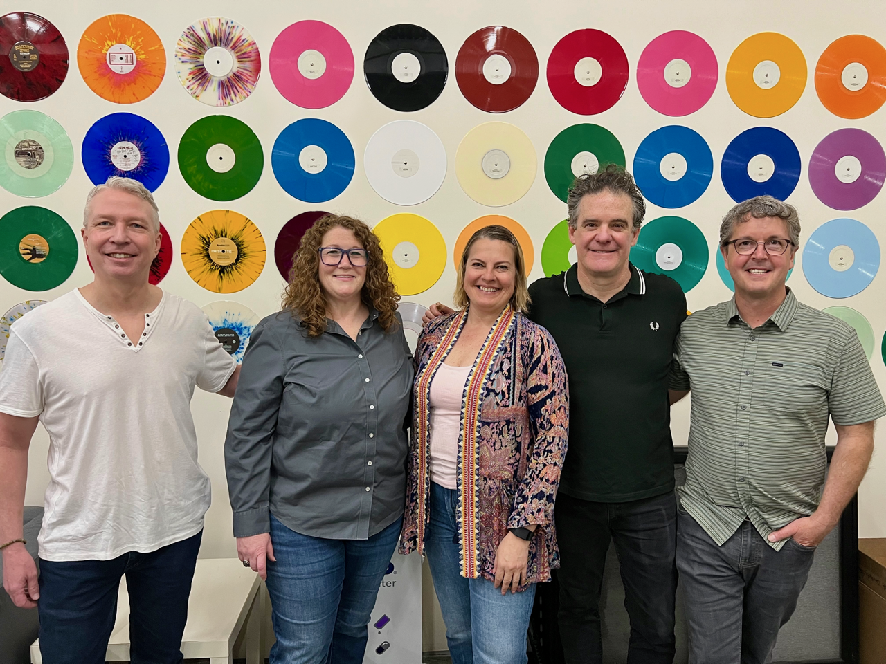 Five people stand todagether agains a wall of colorful vinyl records.