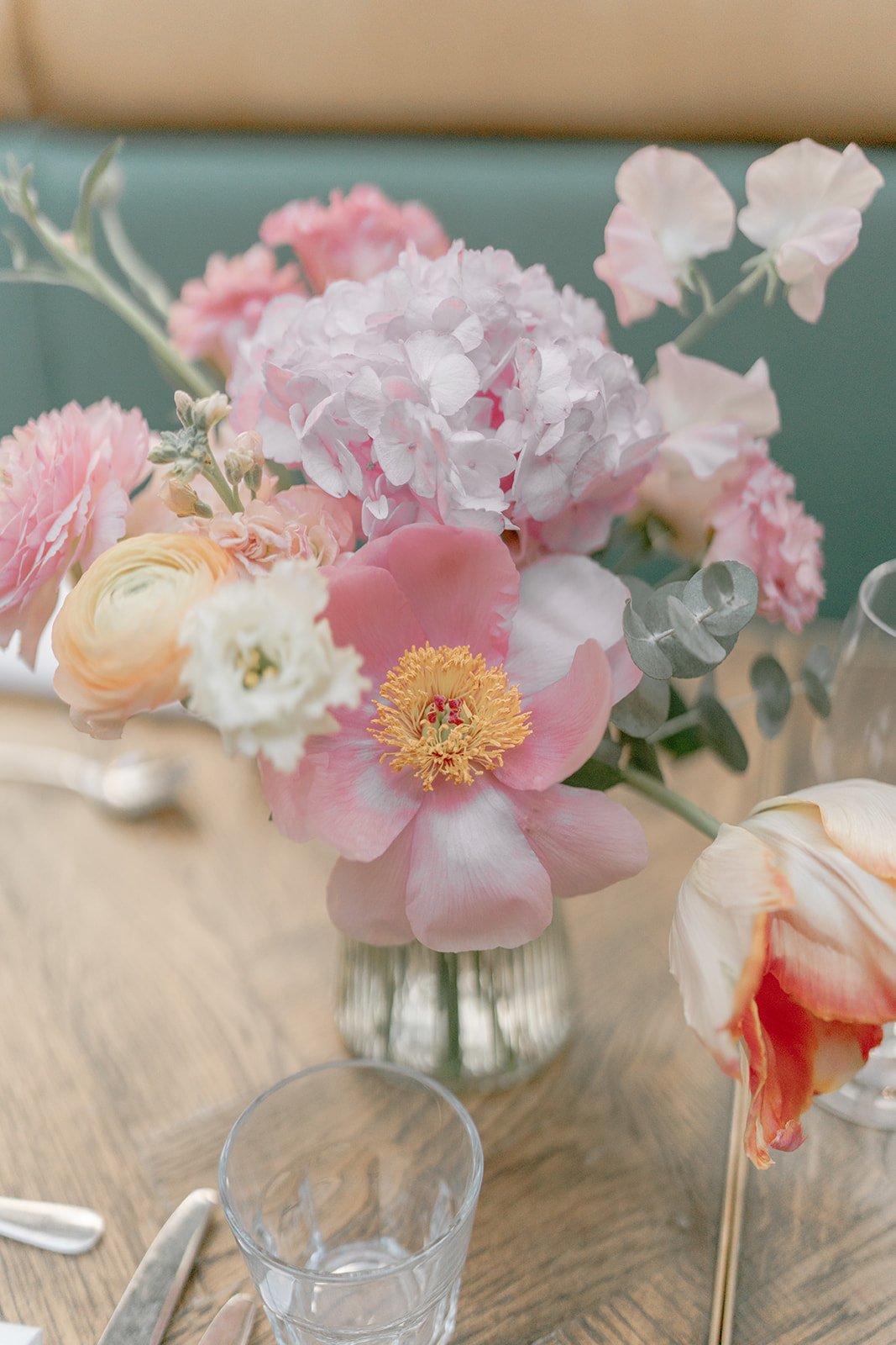 A close-up of a bouquet of pink, white, and peach flowers in a glass vase on a table.