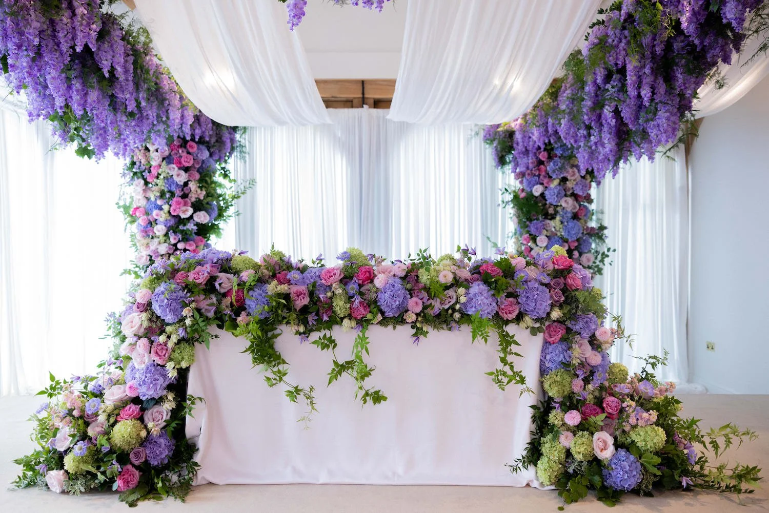 A luxury wedding reception, surrounded by florals, and wisteria decorations hanging from the ceiling.
