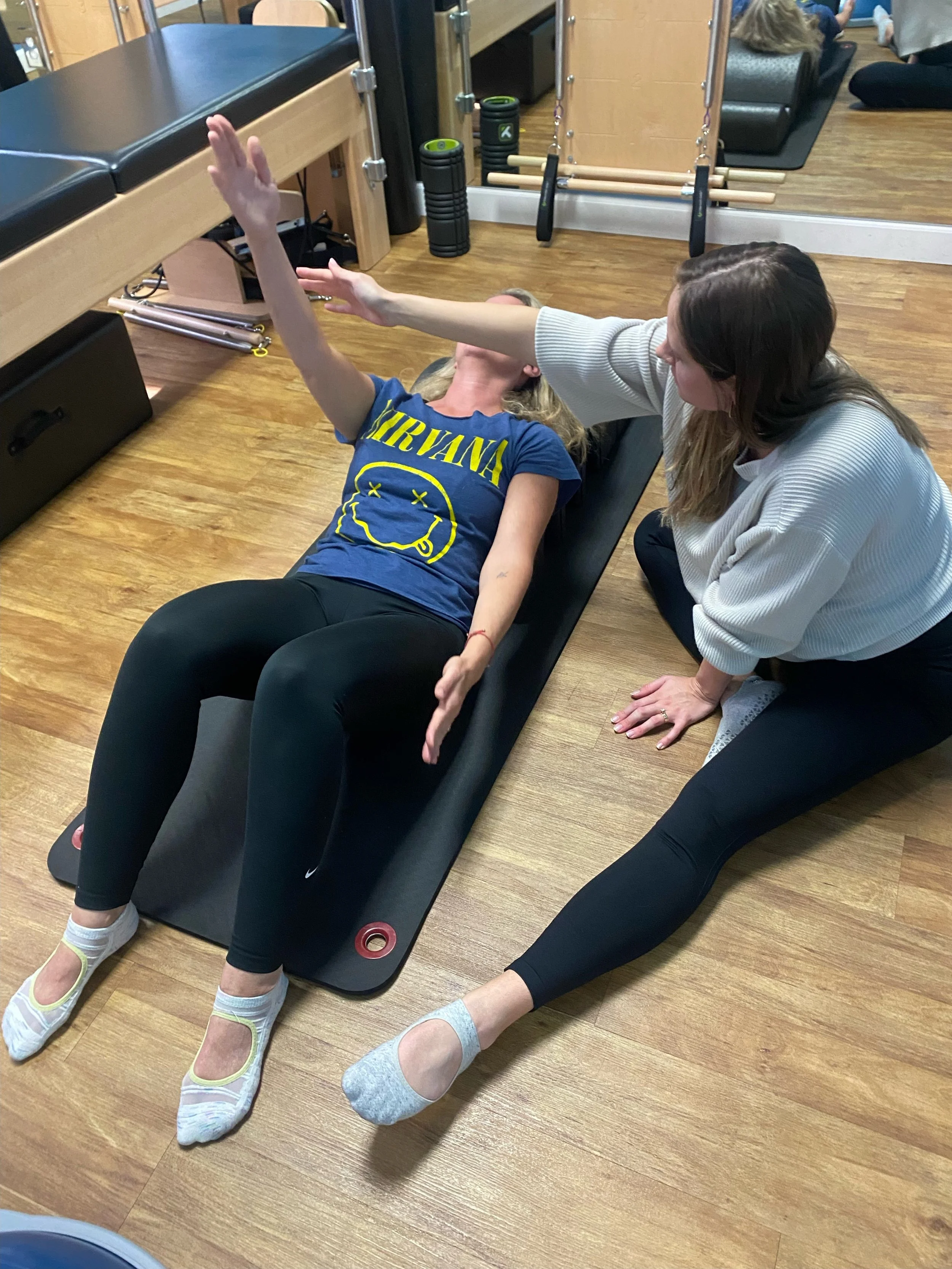 Physical therapy session with one woman lying on a mat and another woman assisting her with arm movements.