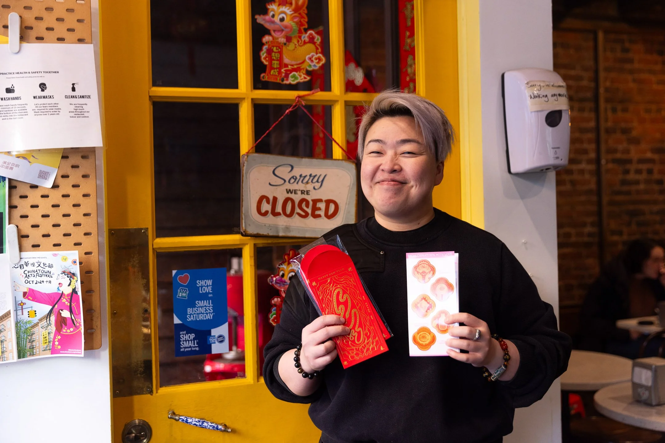 Smiling person holding red and orange Chinese New Year red envelopes and stickers at the shop.
