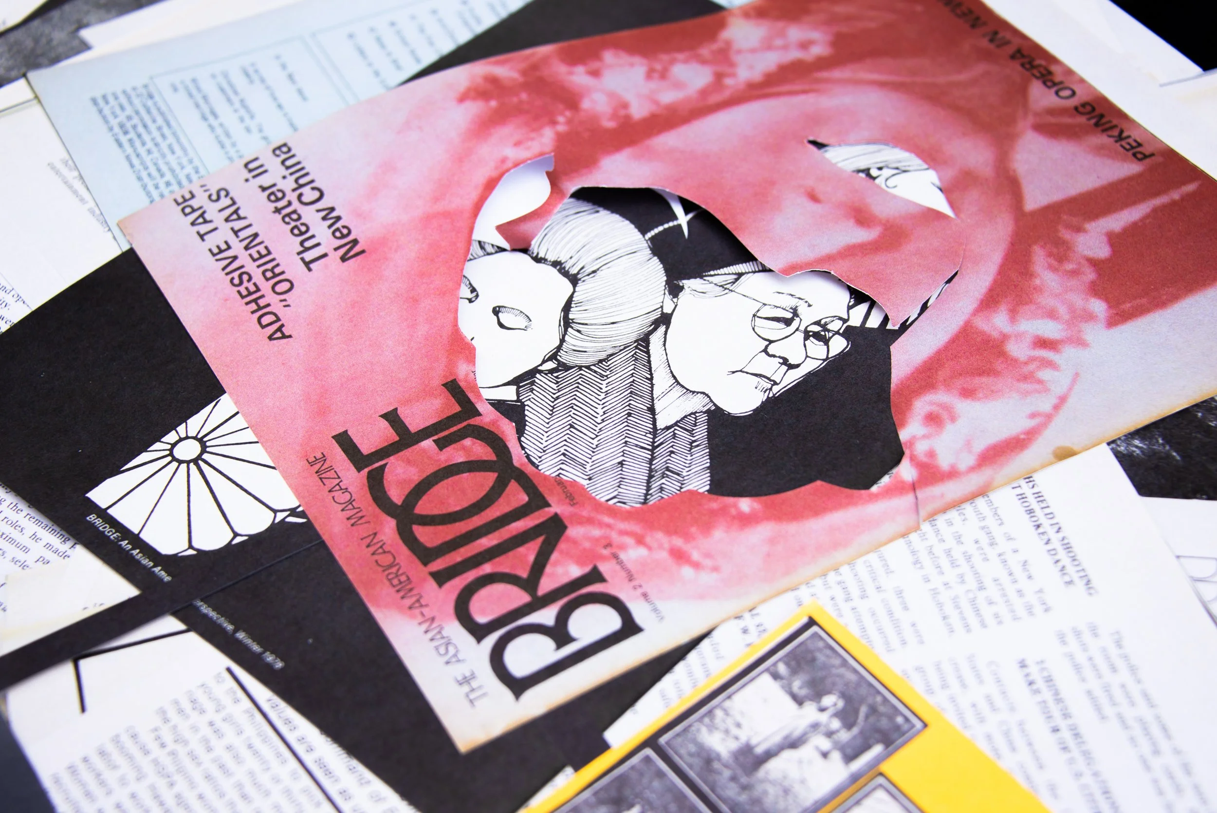 A collage of posters on a table, including a pink poster with a cut-out of lips revealing an illustration of two person's faces.