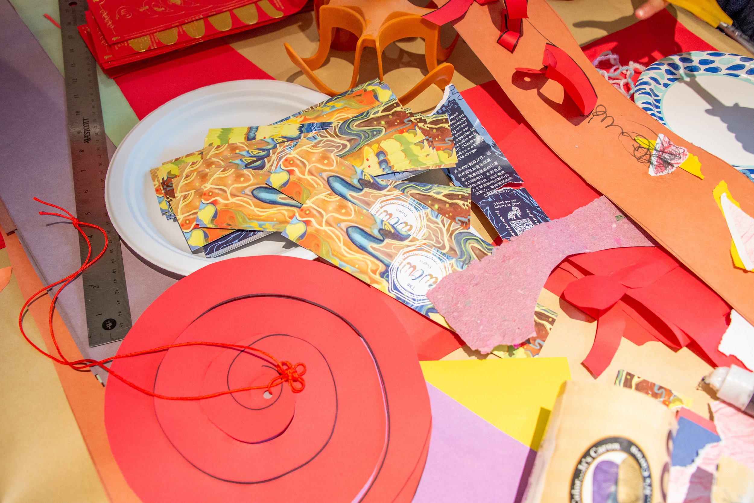 Colorful arts and crafts materials including paper plates, torn paper, ribbon, and paper cutouts scattered on a table.